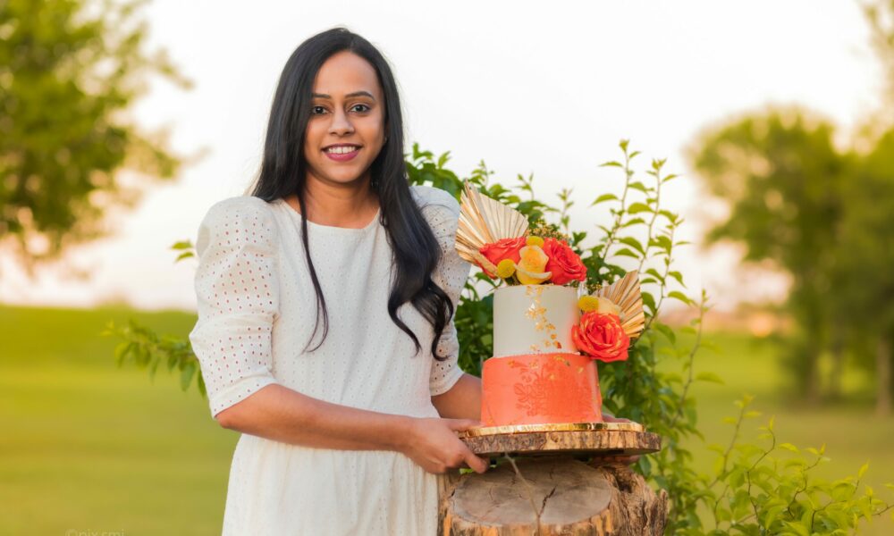 confectioner housewife (pastry-cook) decorate appetizing creamy white  two-tiered wedding cake with fresh flowers on a table with a lace  tablecloth and holds a whisk in studio on a blue background Stock Photo |