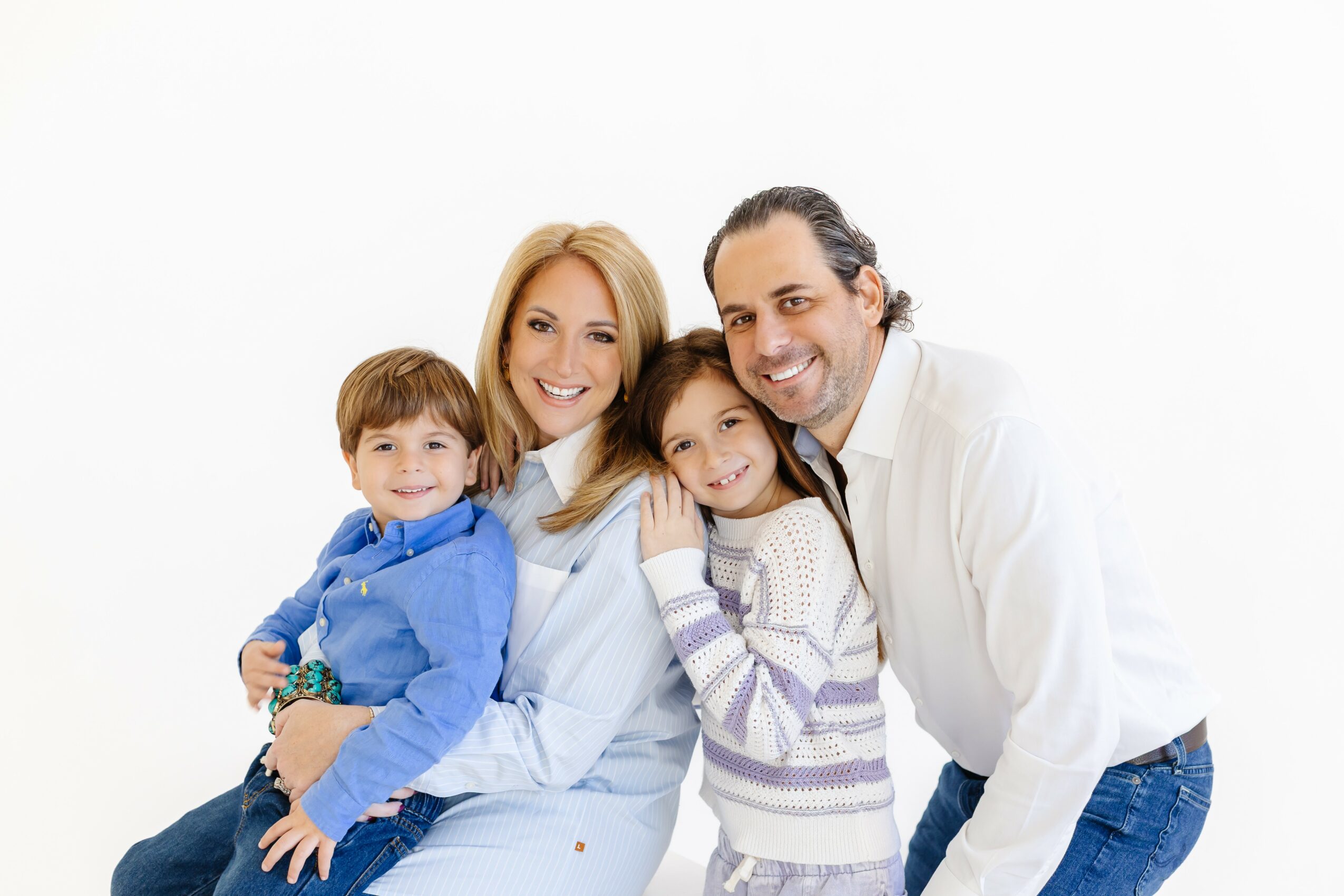 Family of four smiling, standing close together against a white background.