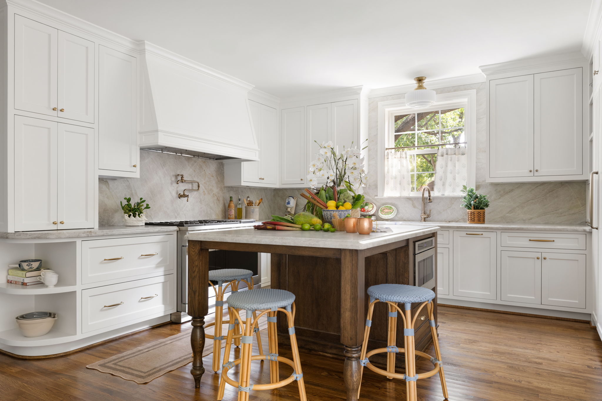 Kitchen with white cabinets, a wooden island, two bar stools, and a window with plants outside.