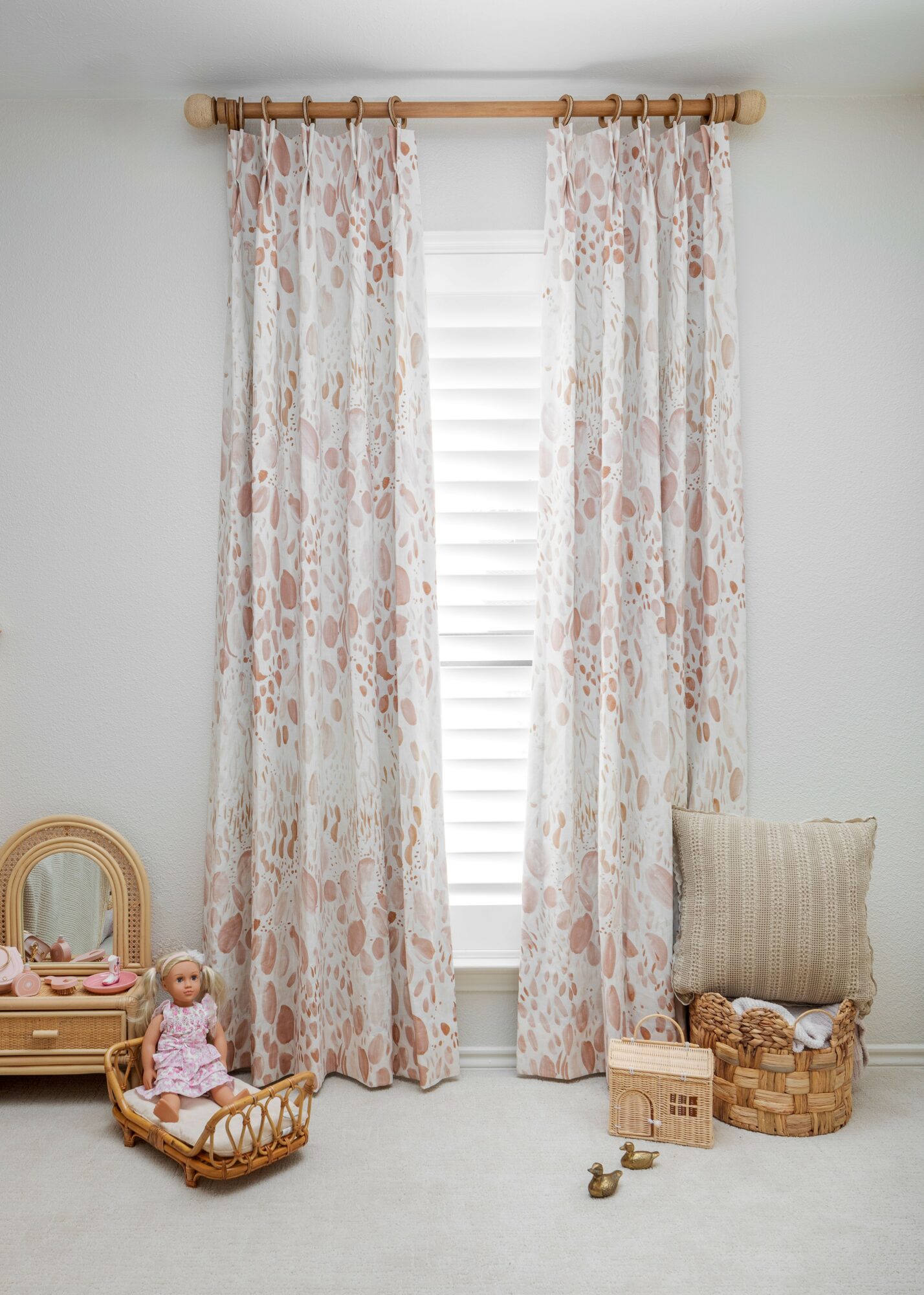 Curtains with floral pattern covering a window with blinds, in a room with toys and a basket on the floor.