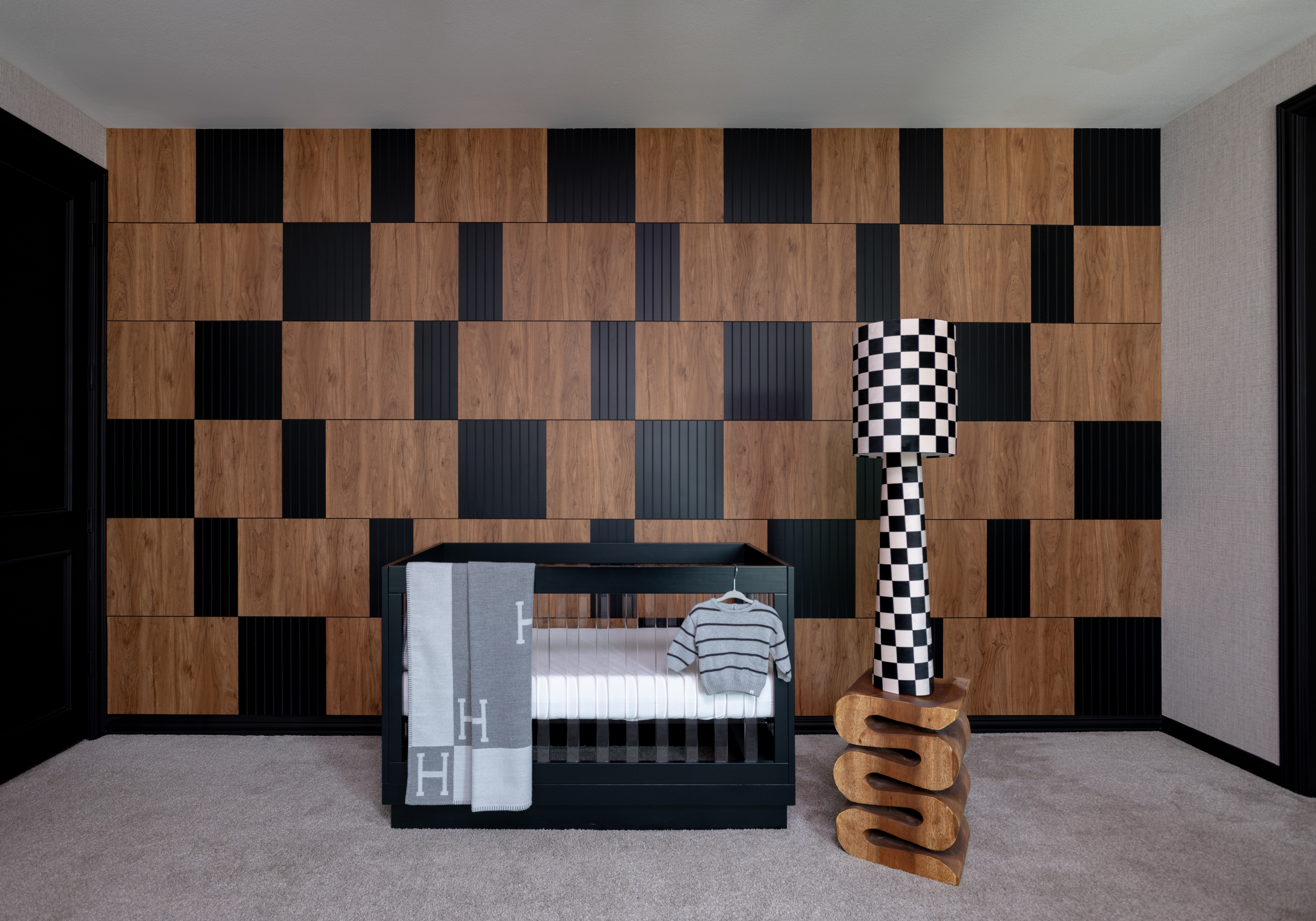 Room with a patterned wooden wall, crib, and a checkered sculpture on a wooden stand.