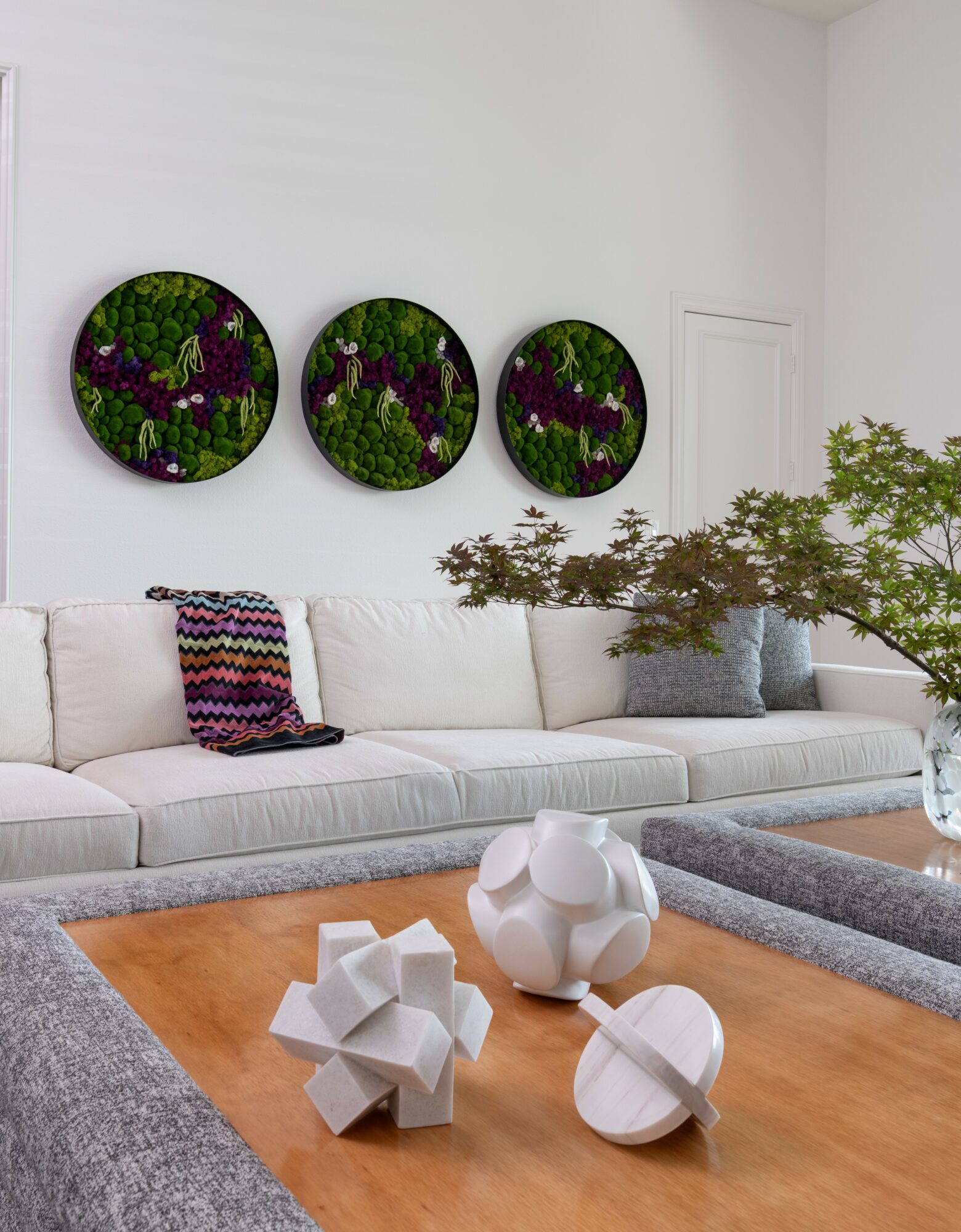 Living room with white sofa, colorful pillows, three circular floral wall art, and a wooden coffee table with decorative objects.