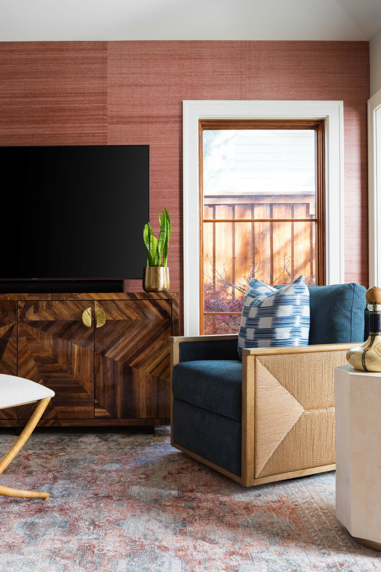 Living room corner with a window, blue sofa, patterned pillows, wooden cabinet, and potted plant.