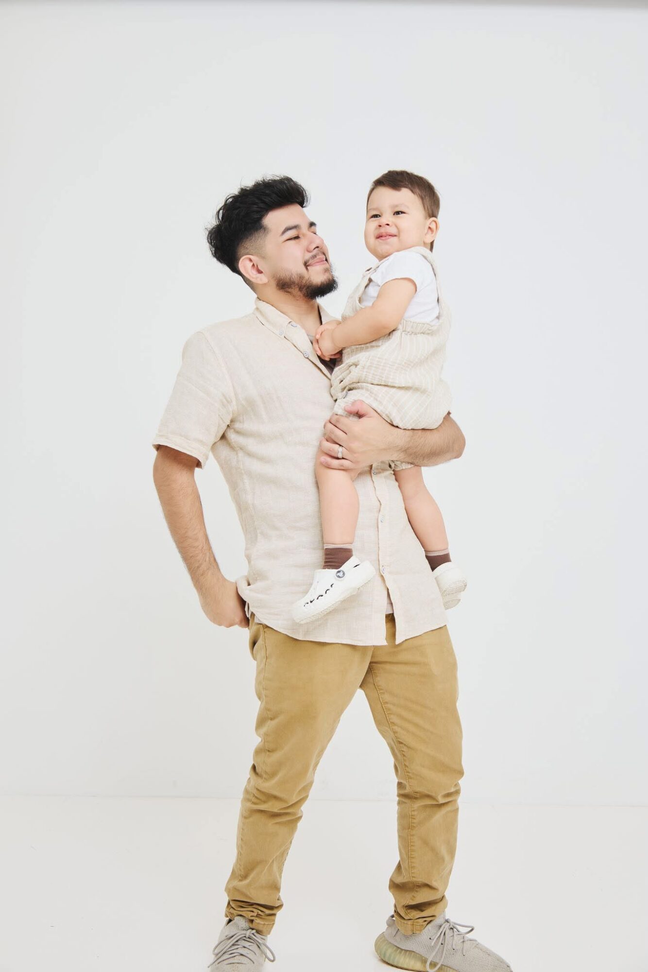 Man holding a smiling child in a white room, both looking at each other.