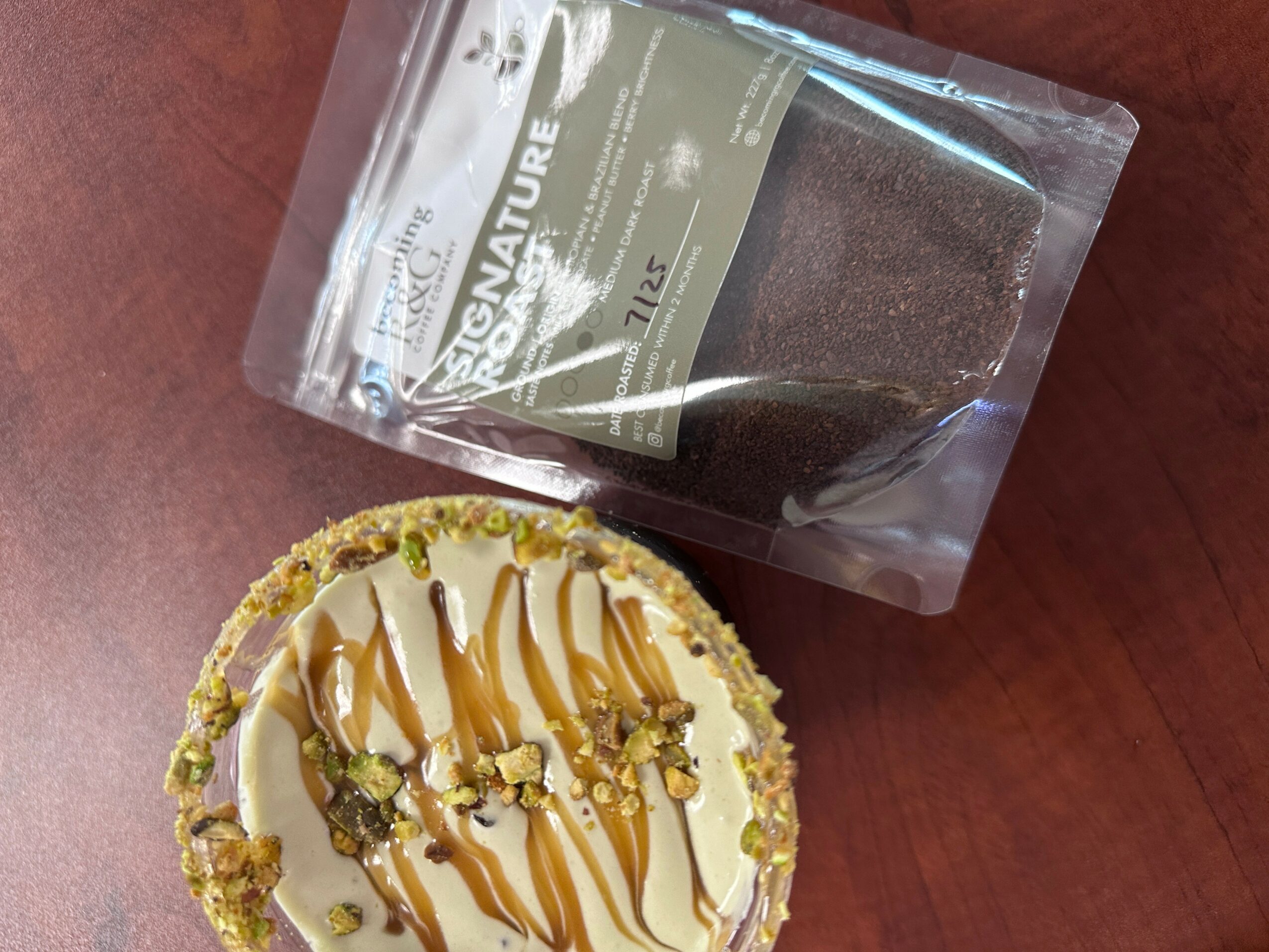 Small dessert with white icing, caramel drizzle, and crushed pistachios on top, placed on a wooden surface.