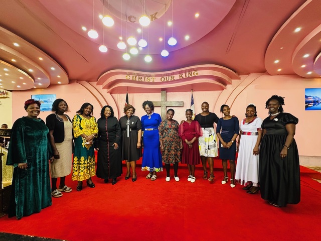 Group of people standing on a red carpet in a decorated room with a cross and banner, posing for a photo.