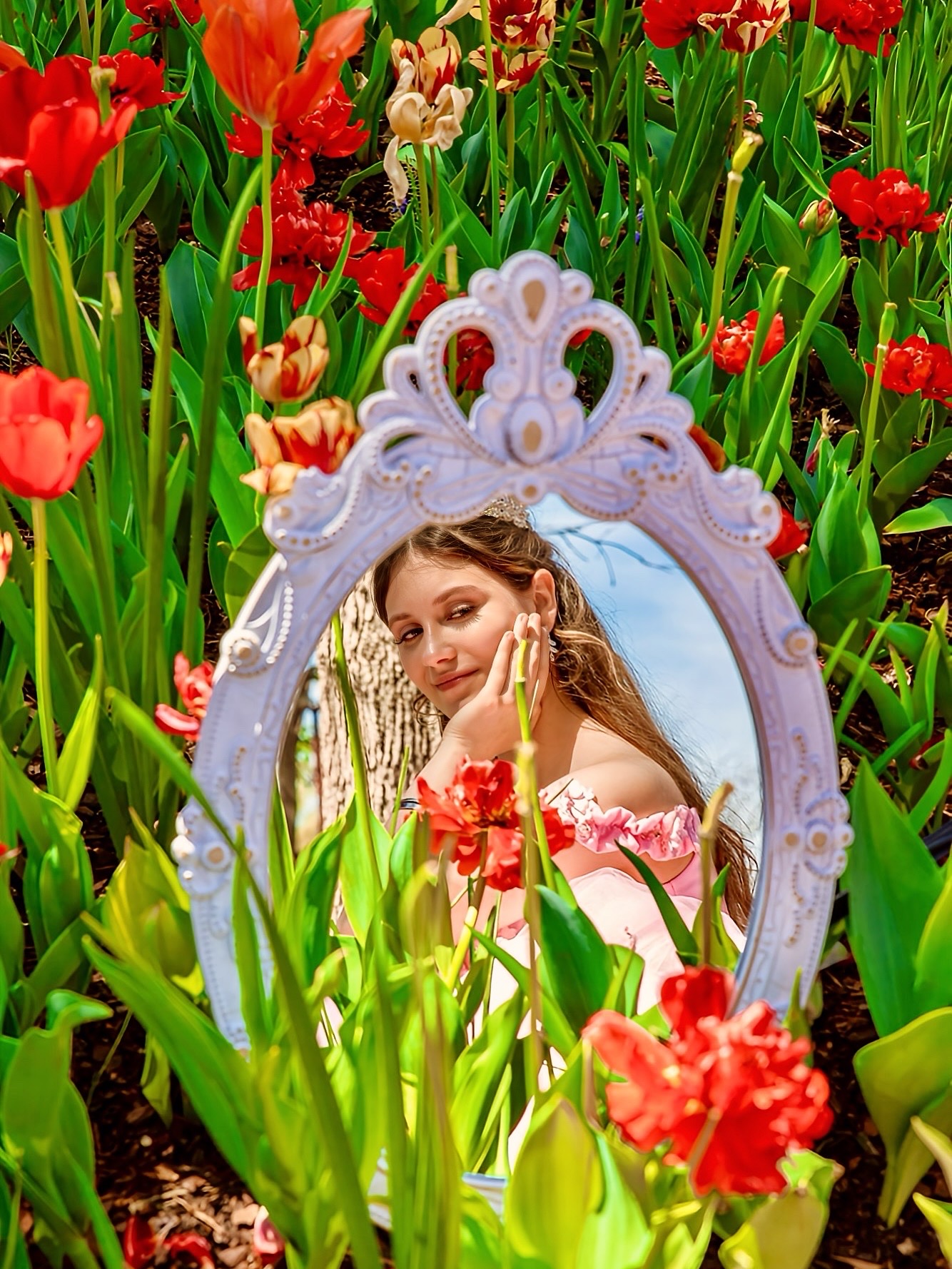 Woman looking at her reflection in an ornate mirror surrounded by colorful tulips and flowers.