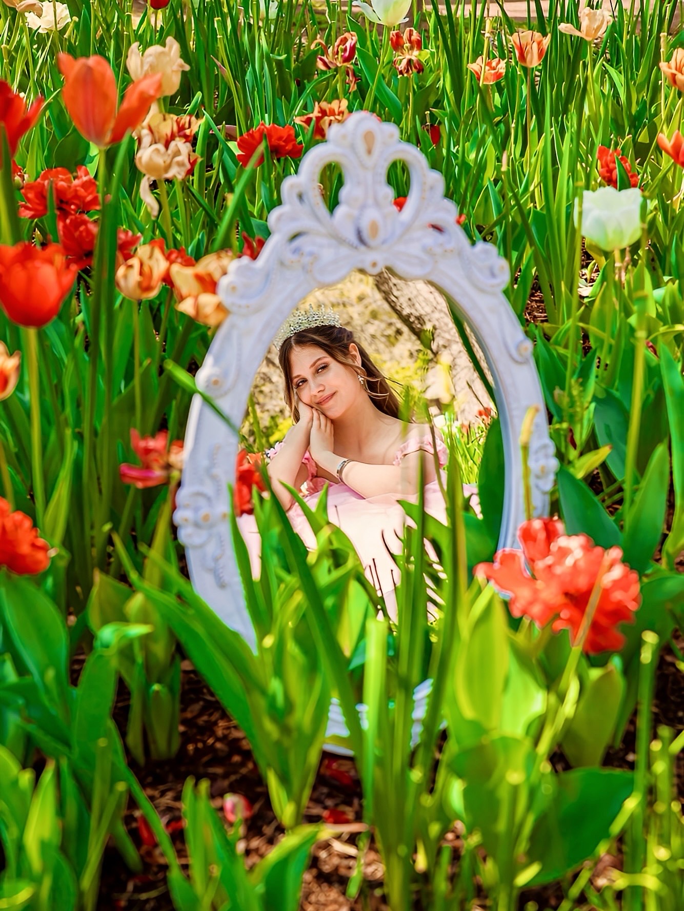 Mirror reflecting a woman in a garden with colorful flowers and green foliage.