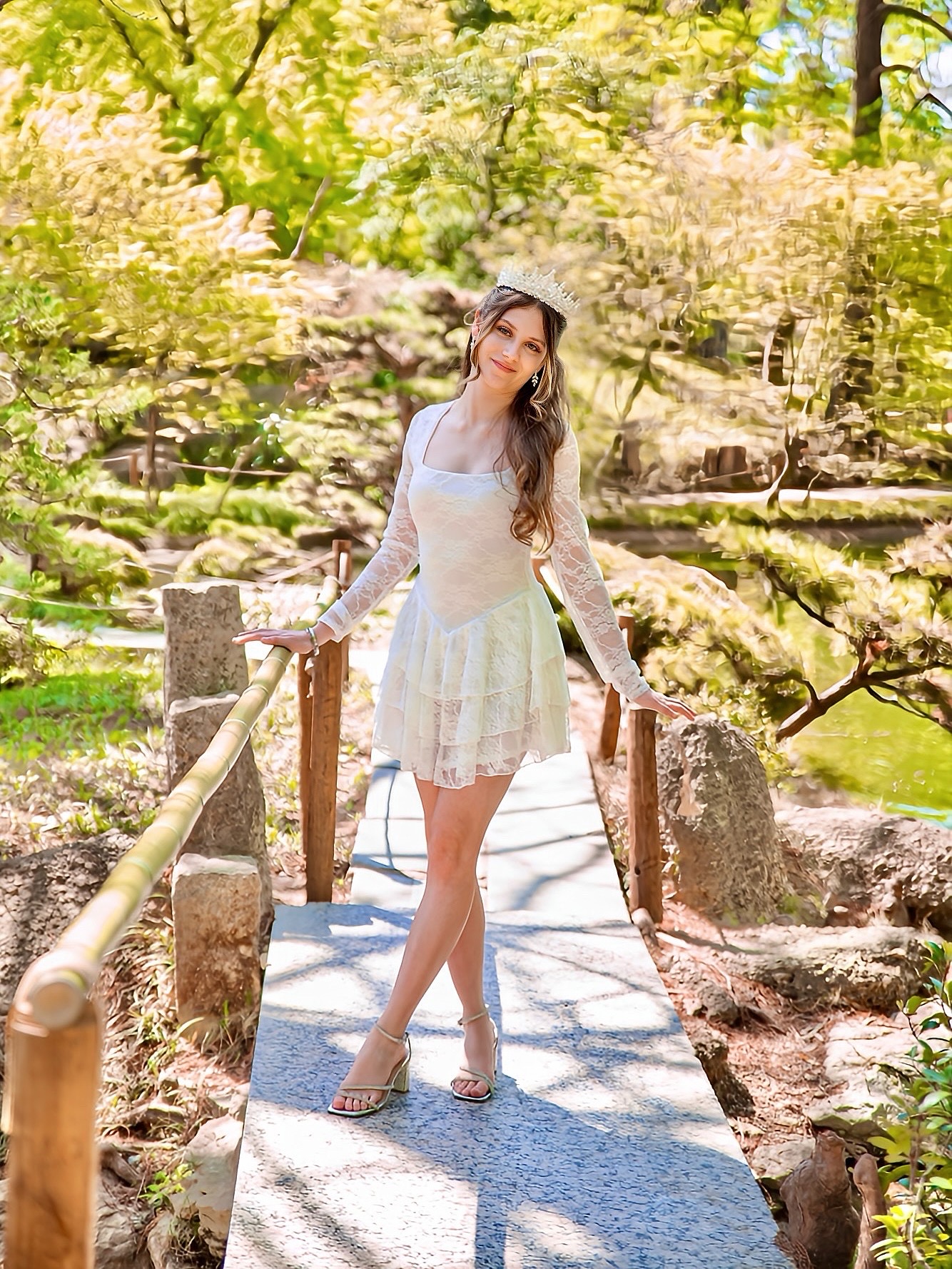 Young woman in a white dress and hat standing on a small bridge in a lush park.
