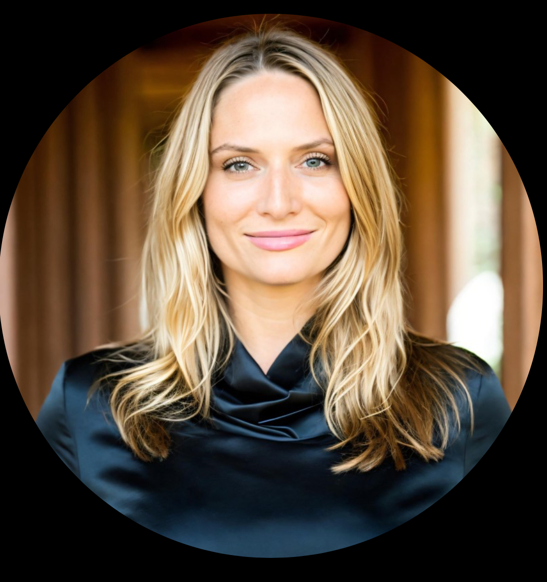 Woman with blonde hair smiling, wearing a dark top, indoors with warm background.