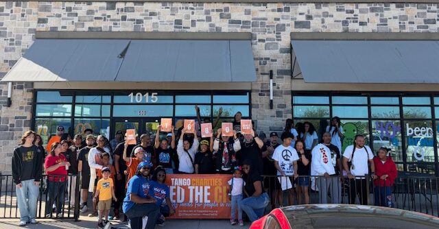 Group of people gathered outside a building holding signs and a banner, some wearing masks.