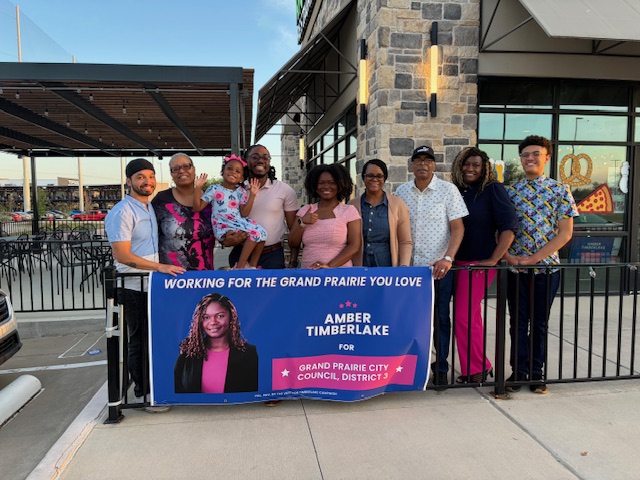 Group of nine people standing outdoors holding a banner for Amber Timberlake, Grand Prairie City Council District 7.