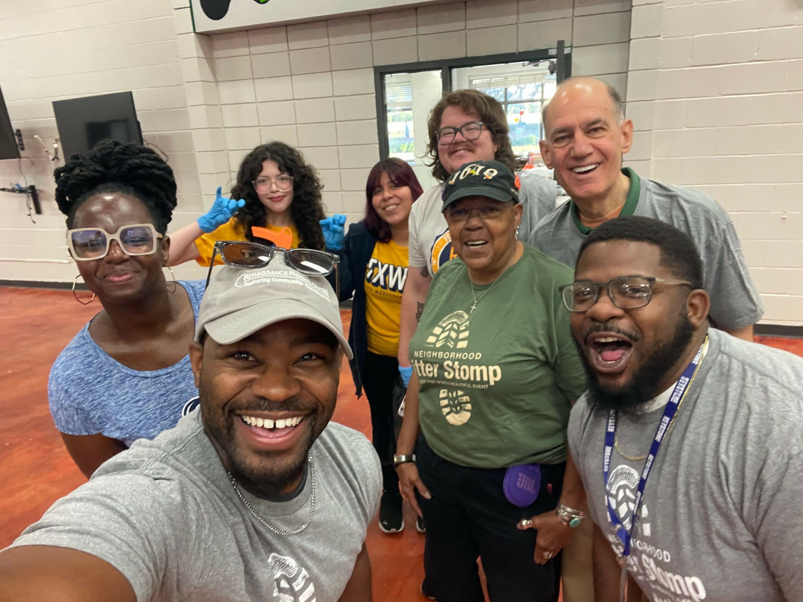 Group of eight diverse people smiling indoors, some wearing glasses and casual clothing, posing for a photo.