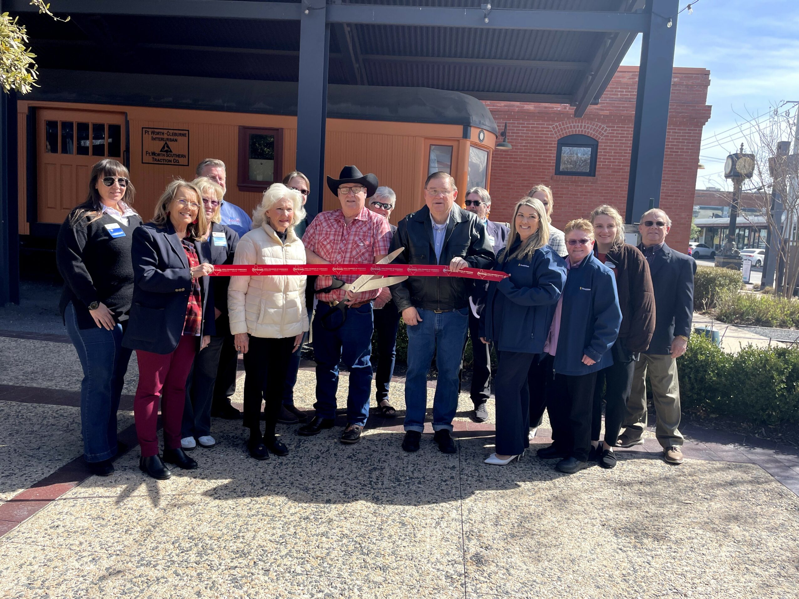 Group of people gathered outdoors for a ribbon-cutting ceremony in front of a building.