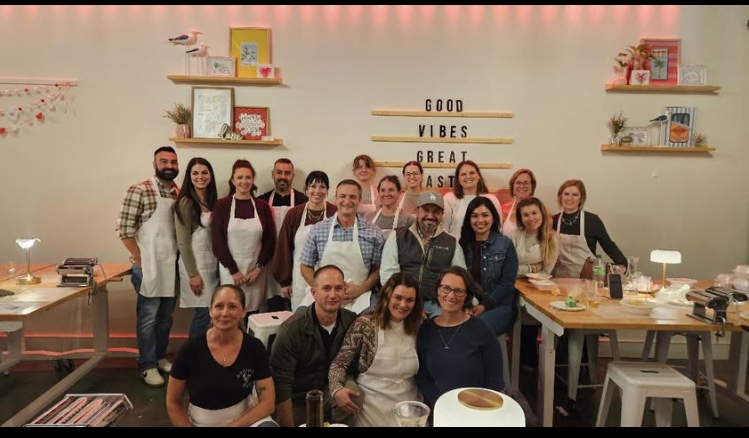 Group of people gathered around a table in a decorated room with shelves and a sign reading 'Good Vibes Great Food'.