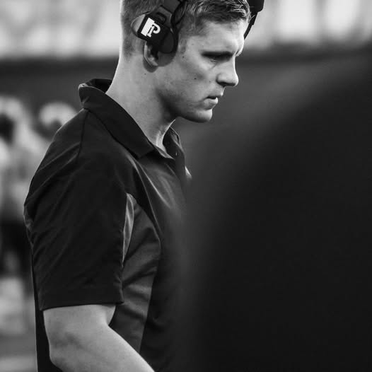 Young man wearing headphones, looking down, in black and white, outdoors, focused expression.