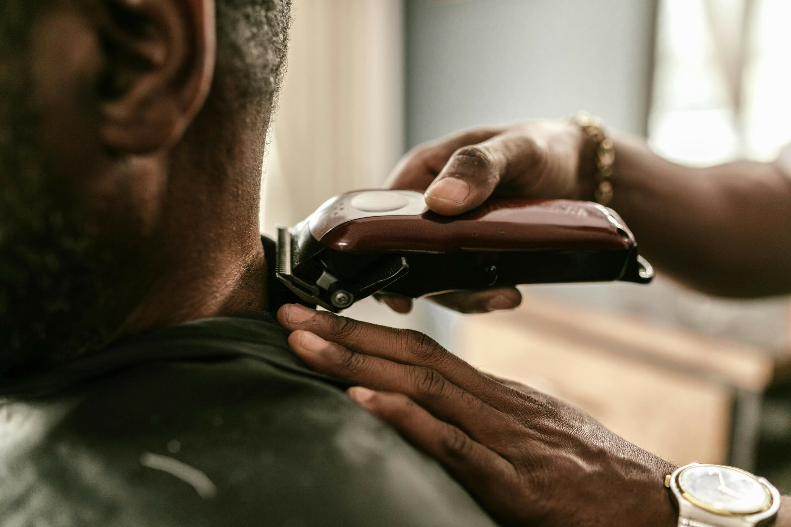 Person receiving a haircut with clippers near the neck, close-up view from behind.