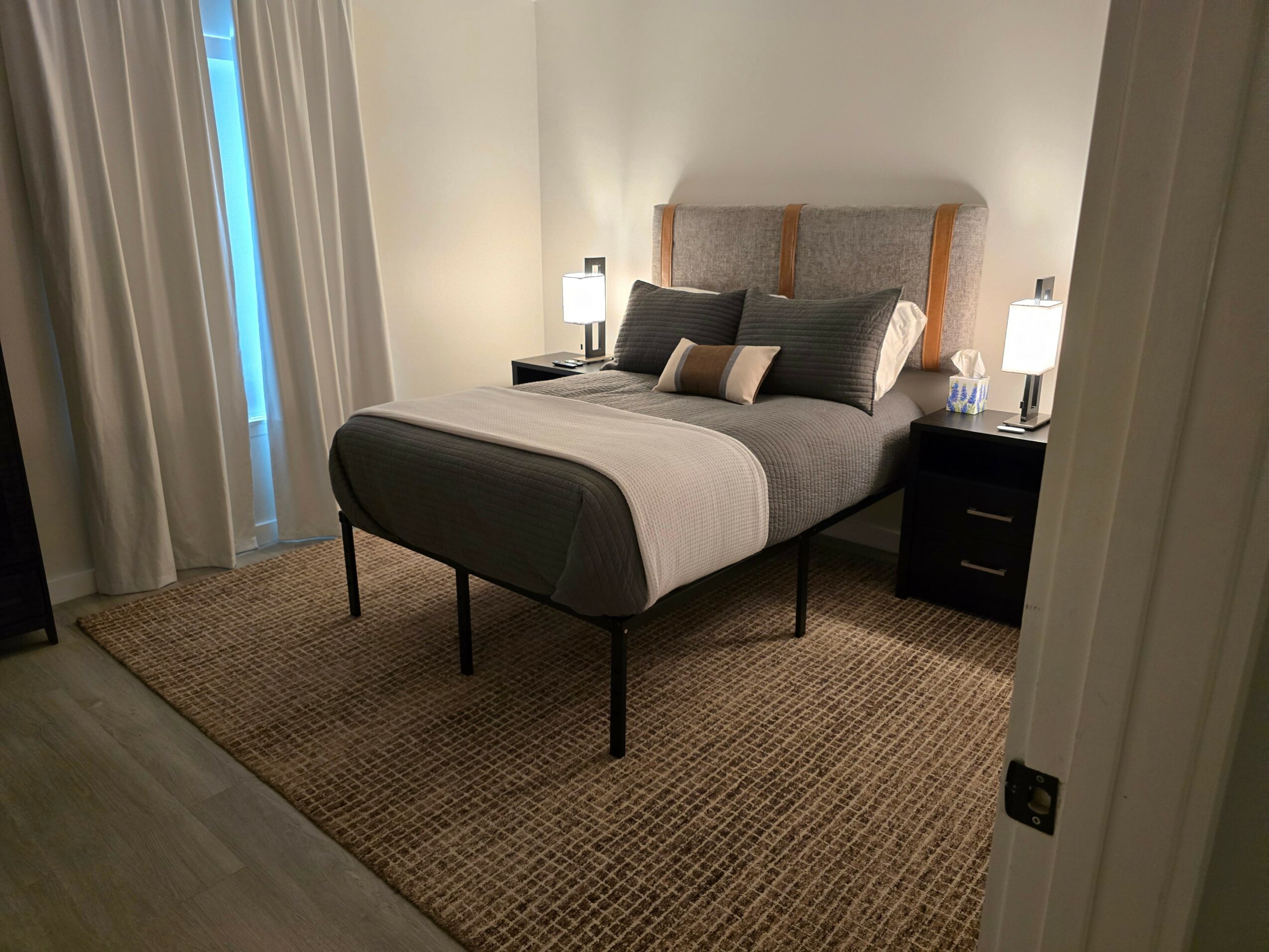 Bedroom with bed, pillows, nightstands, lamps, curtains, and a rug.