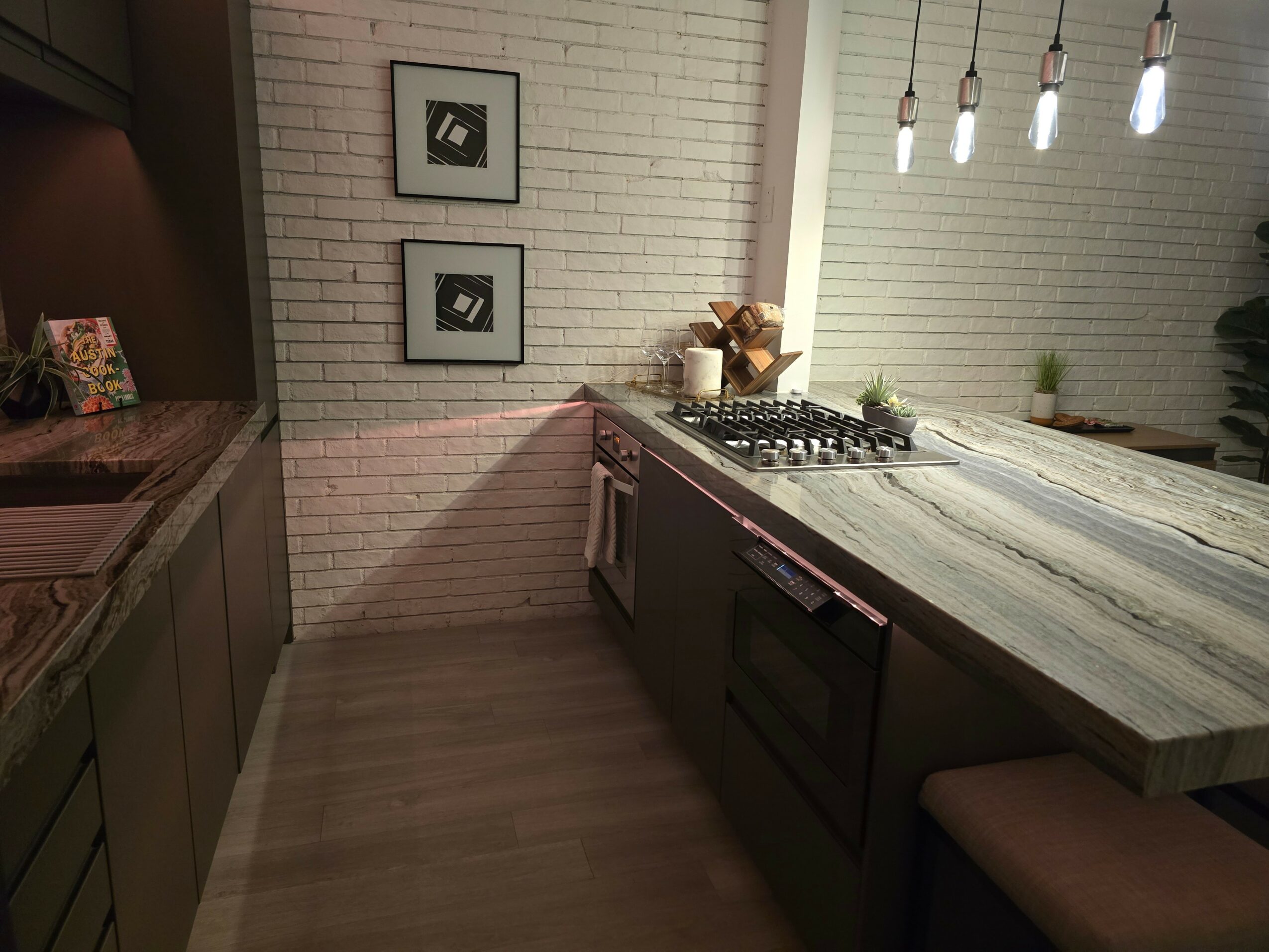 Kitchen with white brick wall, wooden countertop, stove, and hanging lights above a large island.