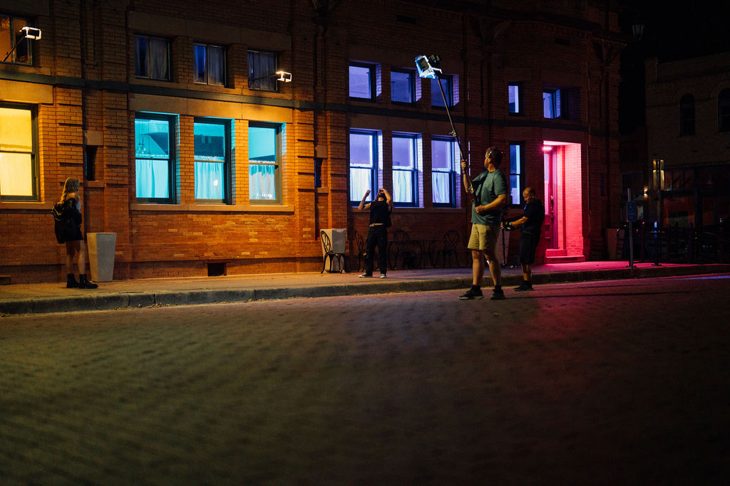 Nighttime street scene with illuminated windows and people walking on sidewalk.