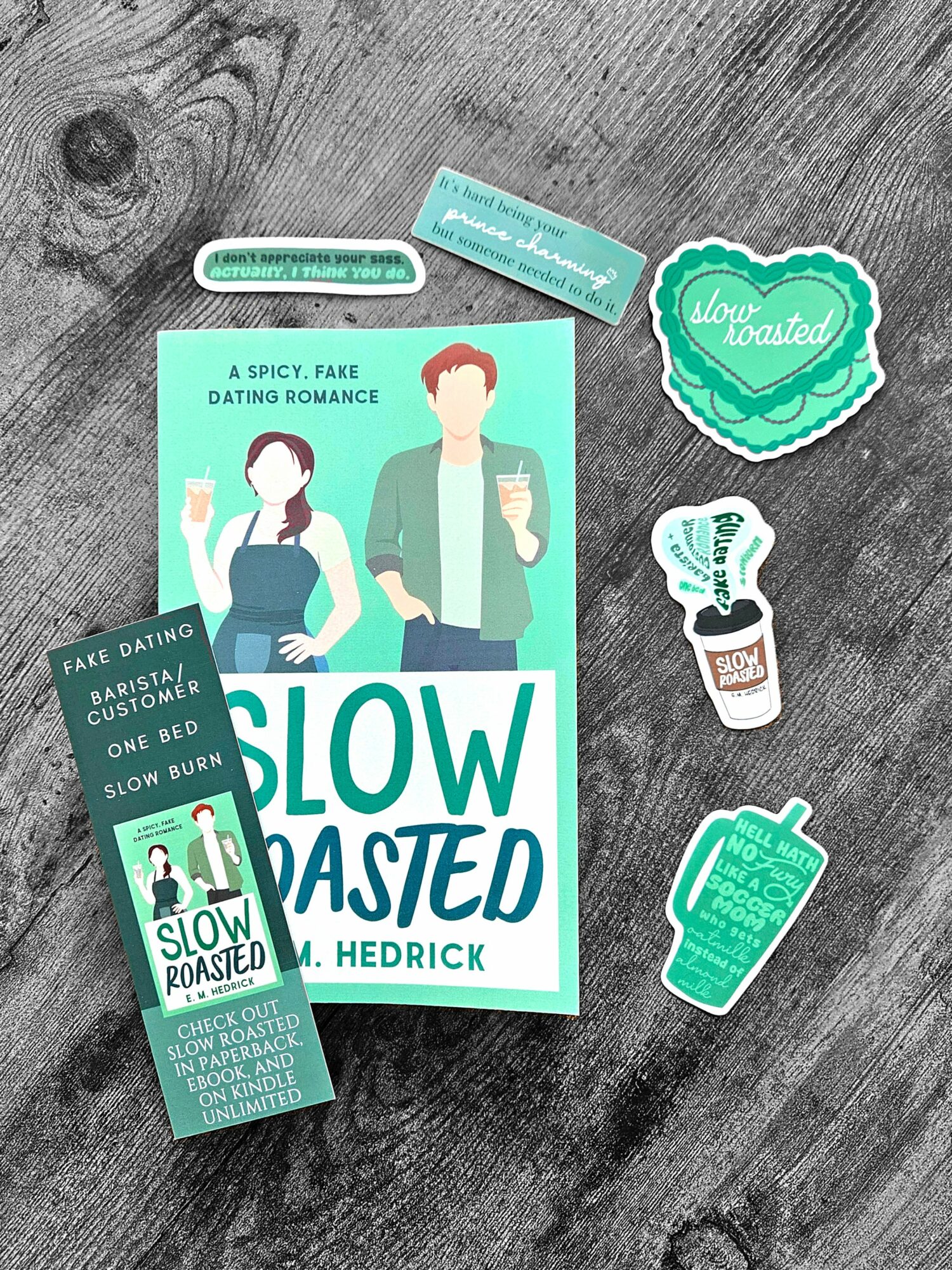 Book titled 'Slow Roasted' with illustrations of a man and woman, surrounded by stickers and a small card, on a wooden surface.