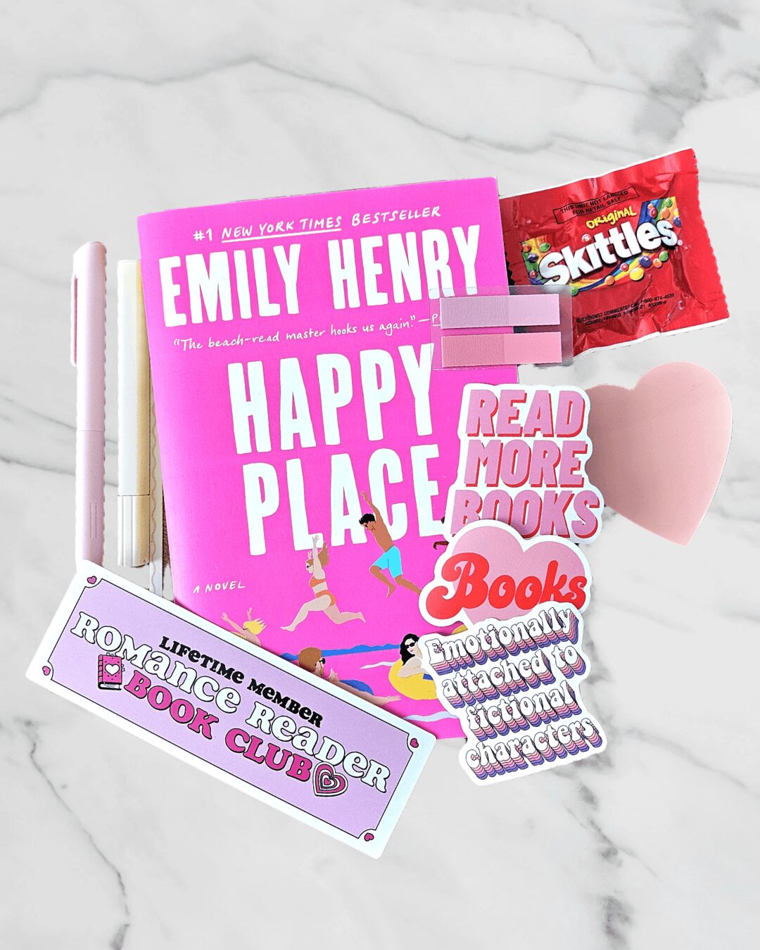 Pink book titled 'Happy Place' with a pink heart, Skittles packet, and various stickers on a marble surface.