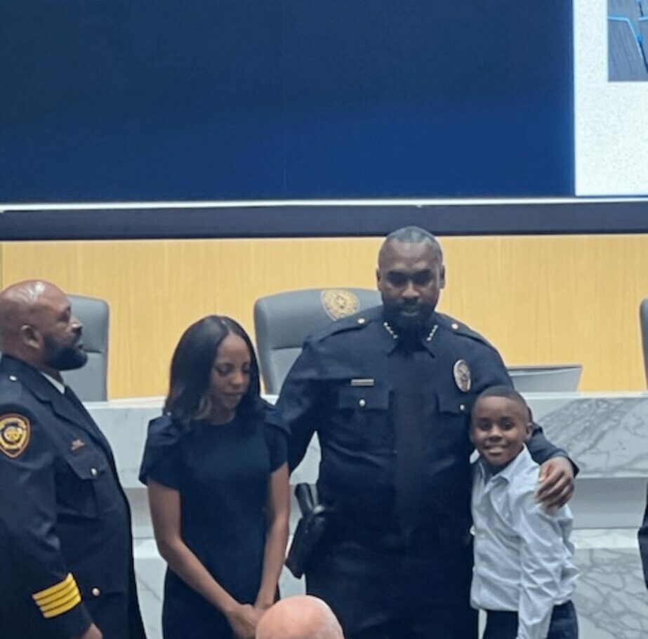 Four people standing together in front of a blue and yellow wall, including two children and two adults in uniform.