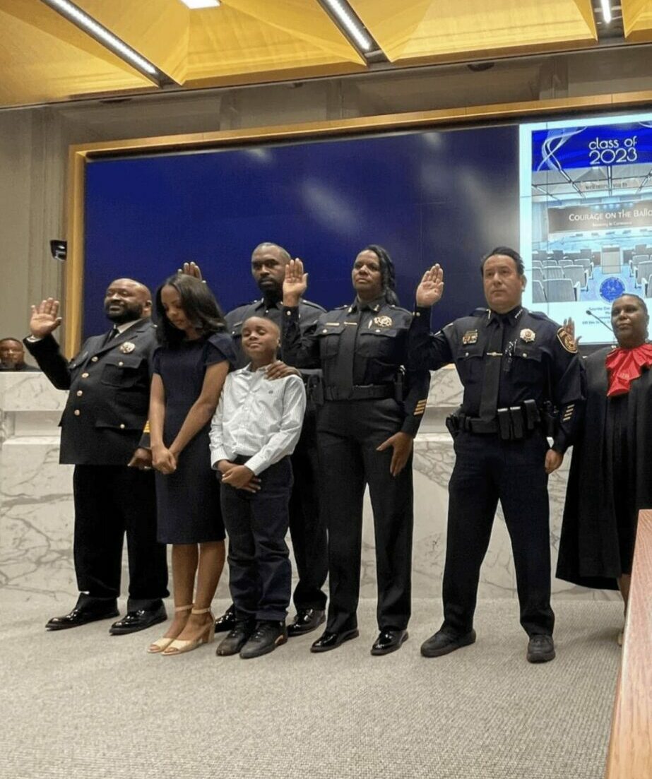 Group of people, including children and adults, standing in a line indoors with a display board behind them.