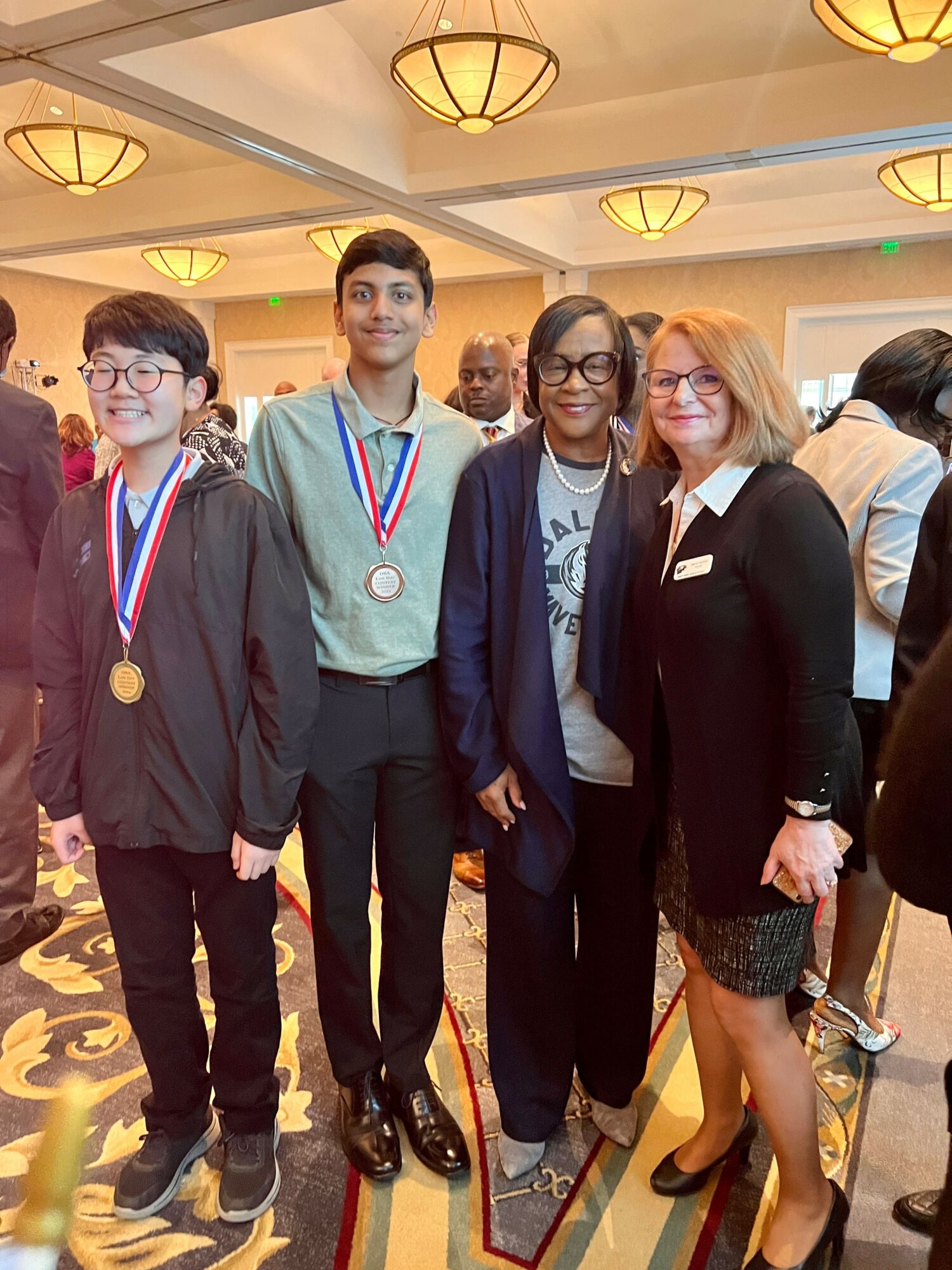 Four people standing together indoors, wearing medals and formal attire, smiling for the photo.