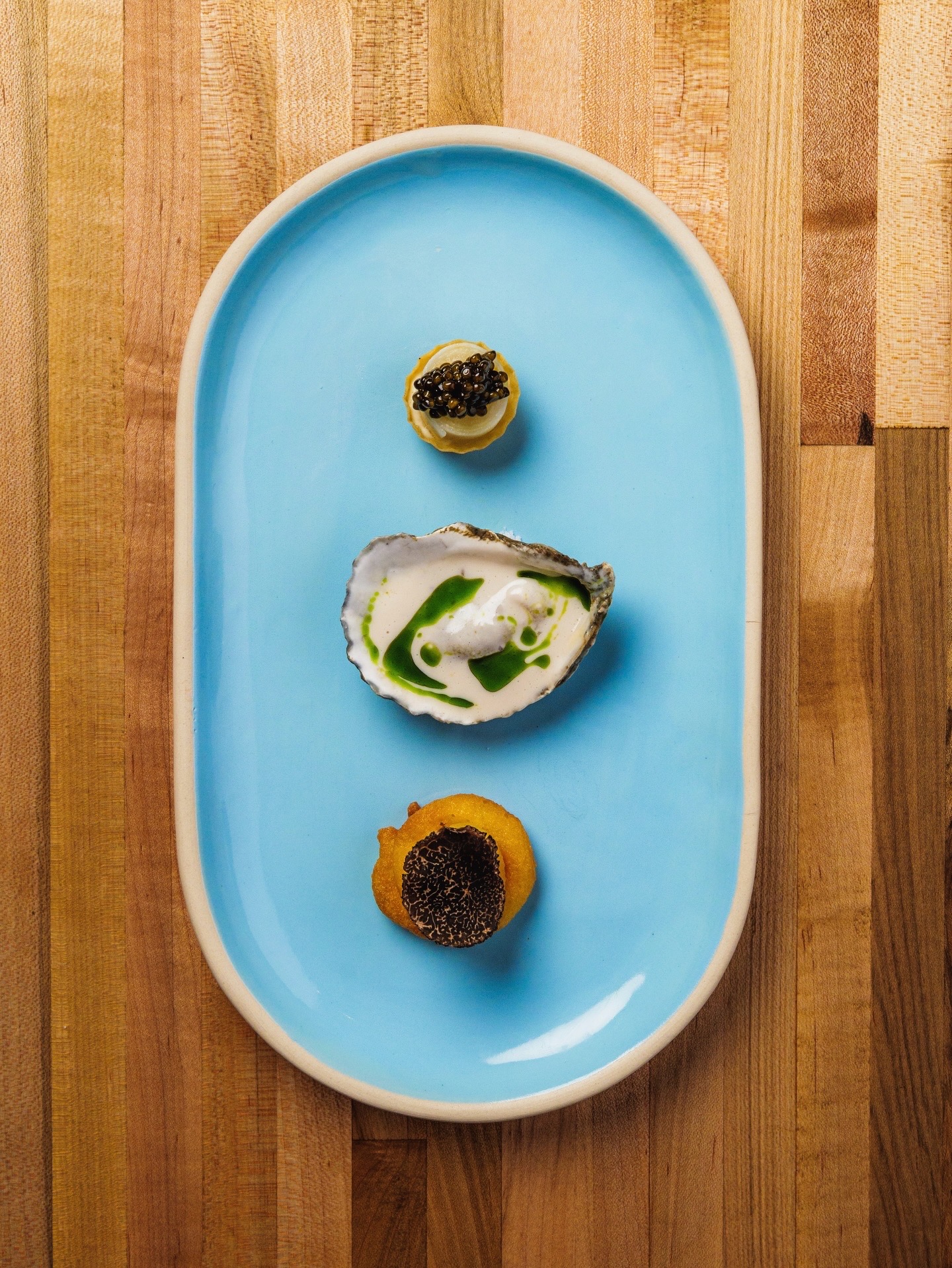 Three small food items on a blue oval plate placed on a wooden surface.