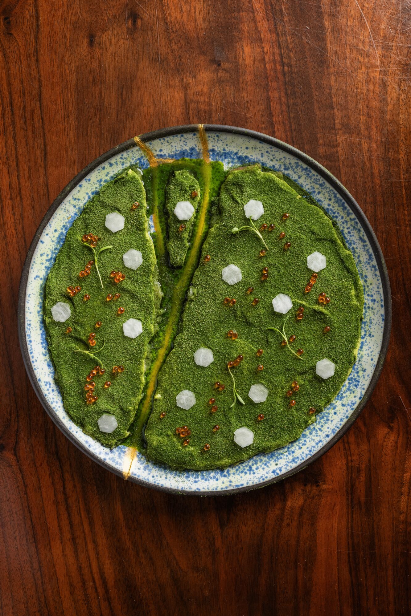 Round plate with green dessert topped with white dots and orange sprinkles, on a wooden surface.
