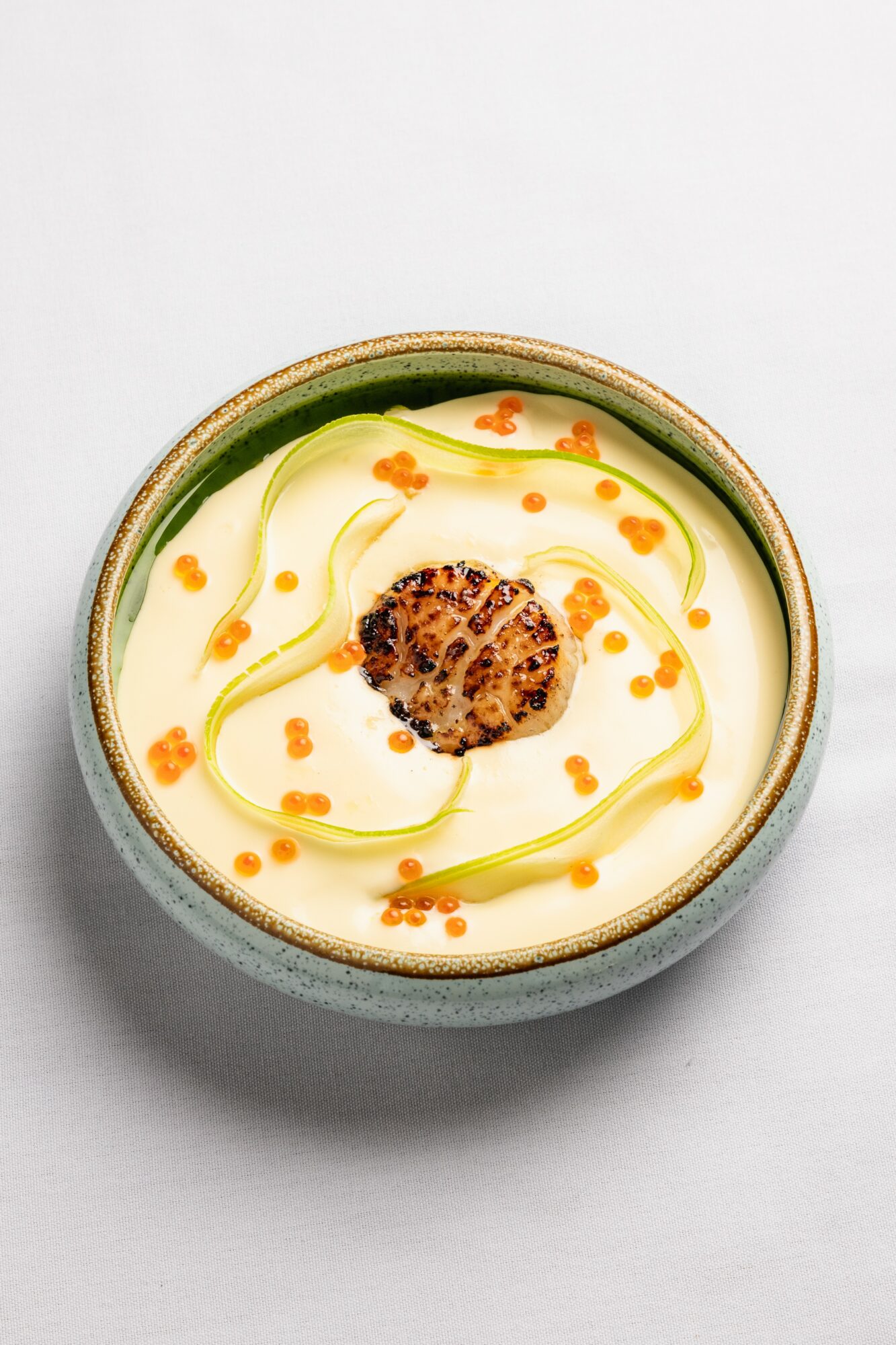 Bowl of creamy dessert with a central nut topping, garnished with orange and green syrup swirls.