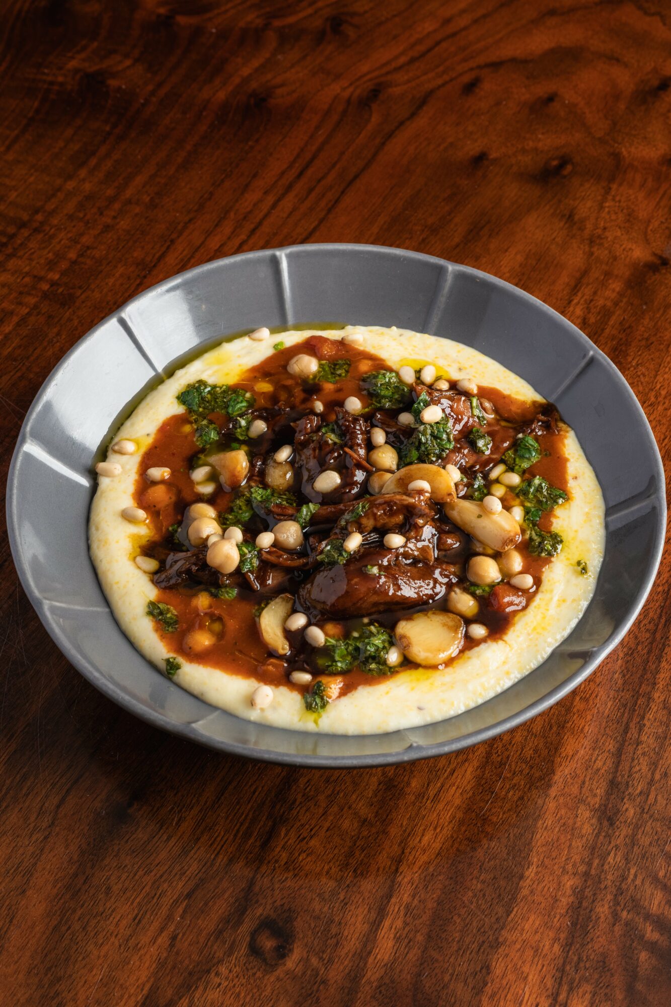 Dish with sauce, vegetables, and beans on a white base in a gray bowl on a wooden table.