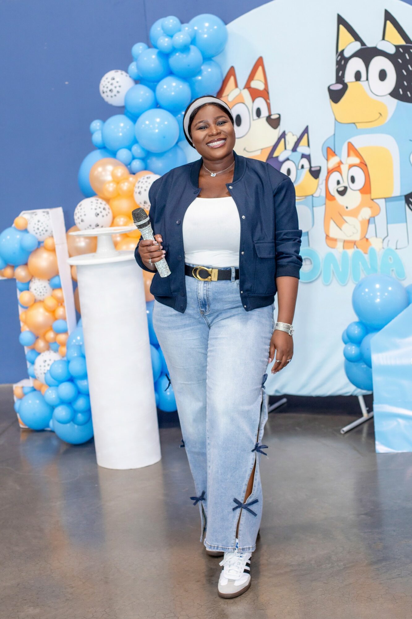 Woman smiling holding a drink at a colorful cartoon-themed party with balloons and character cutouts.