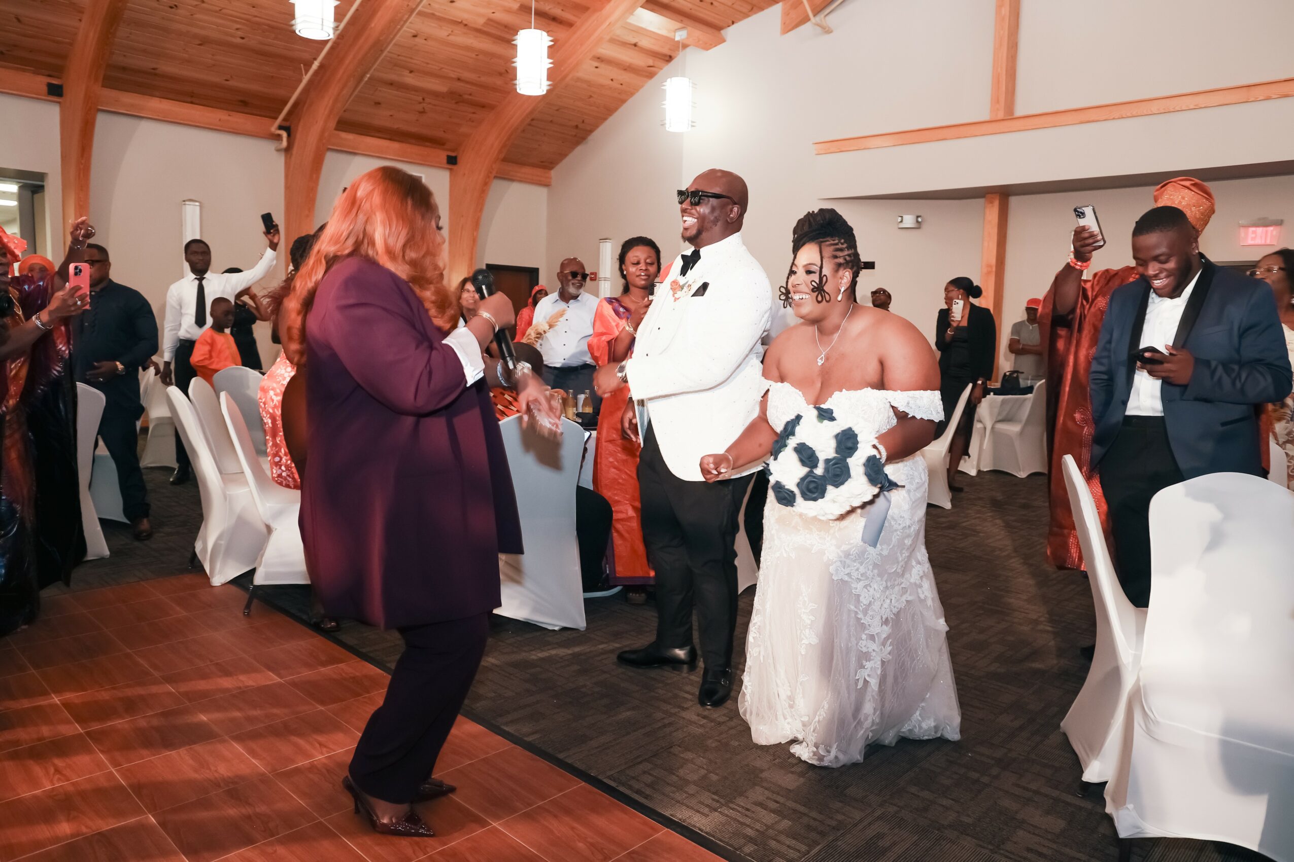 People dancing and socializing in a decorated event hall with wooden ceiling beams and white walls.