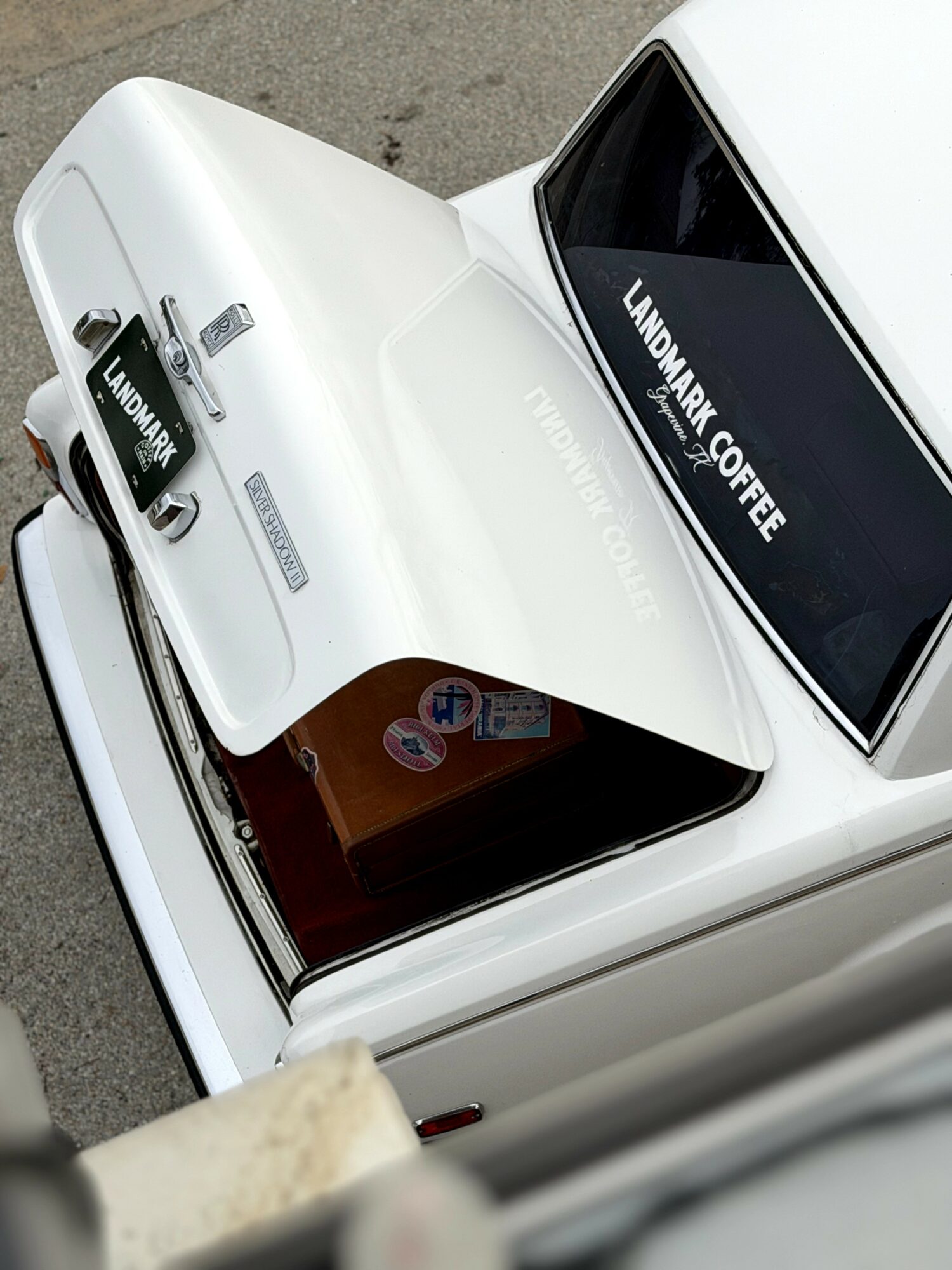White car with a sign reading 'LANDMARK COFFEE' on the windshield, viewed from above.