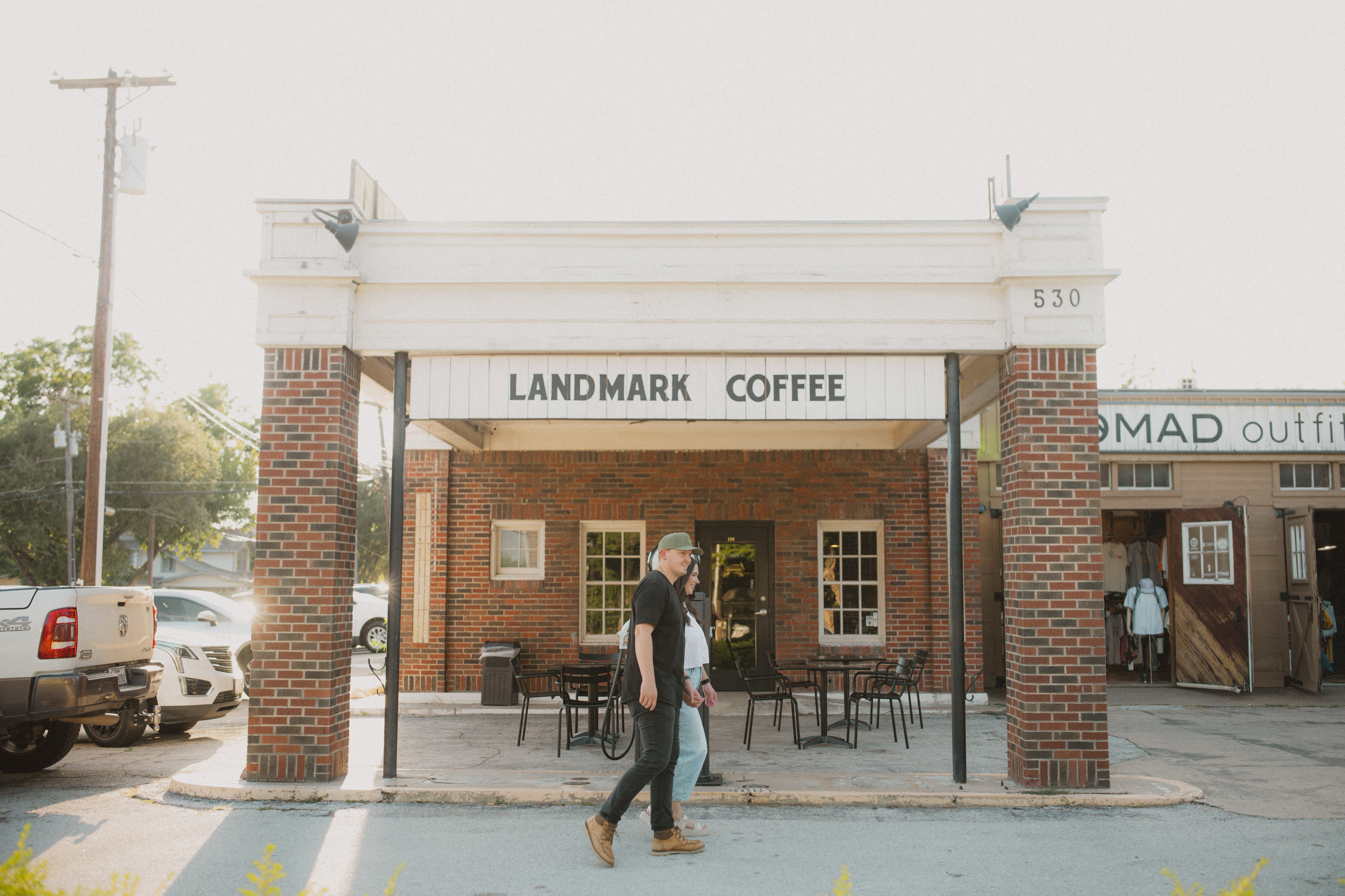Person walking past Landmark Coffee storefront with brick columns and outdoor seating area.