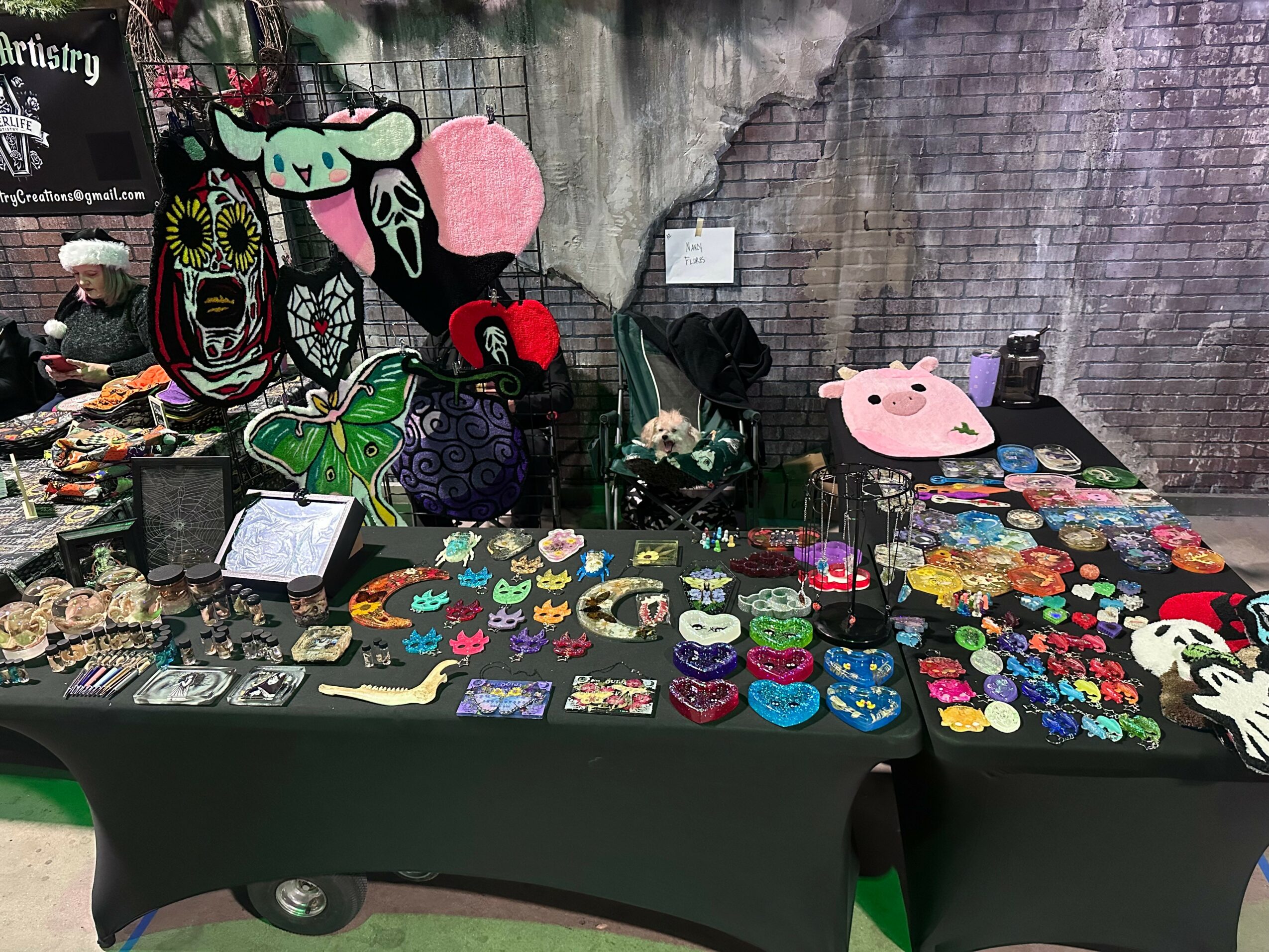 Street vendor table with colorful jewelry, accessories, and plush toys against a graffiti wall background.