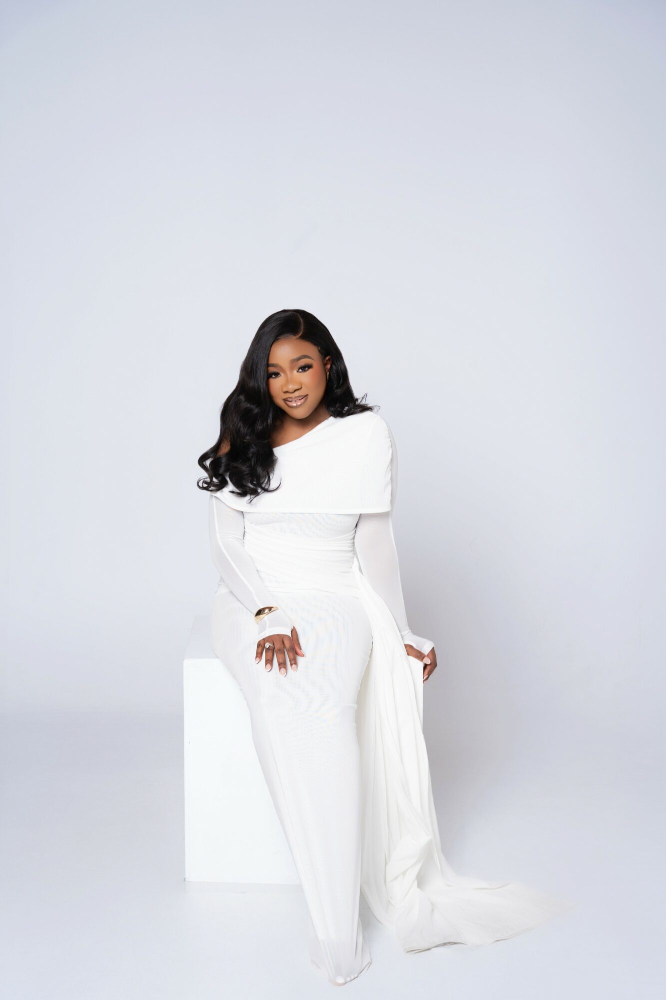 Woman in white dress sitting on a white block against a plain light background.