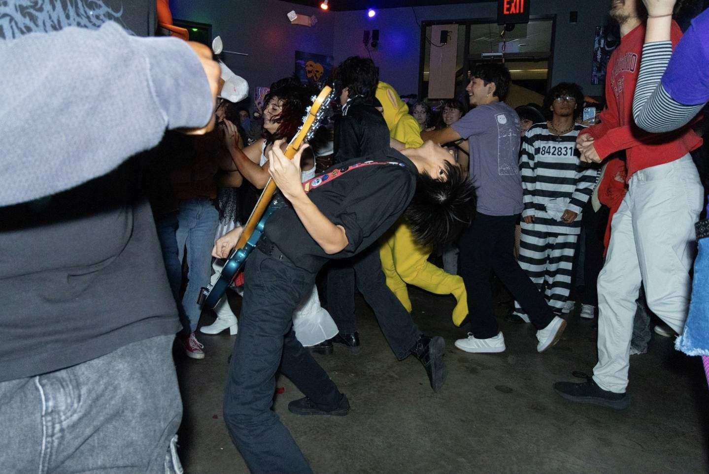 Person playing guitar in a crowded indoor space with people dancing and socializing.