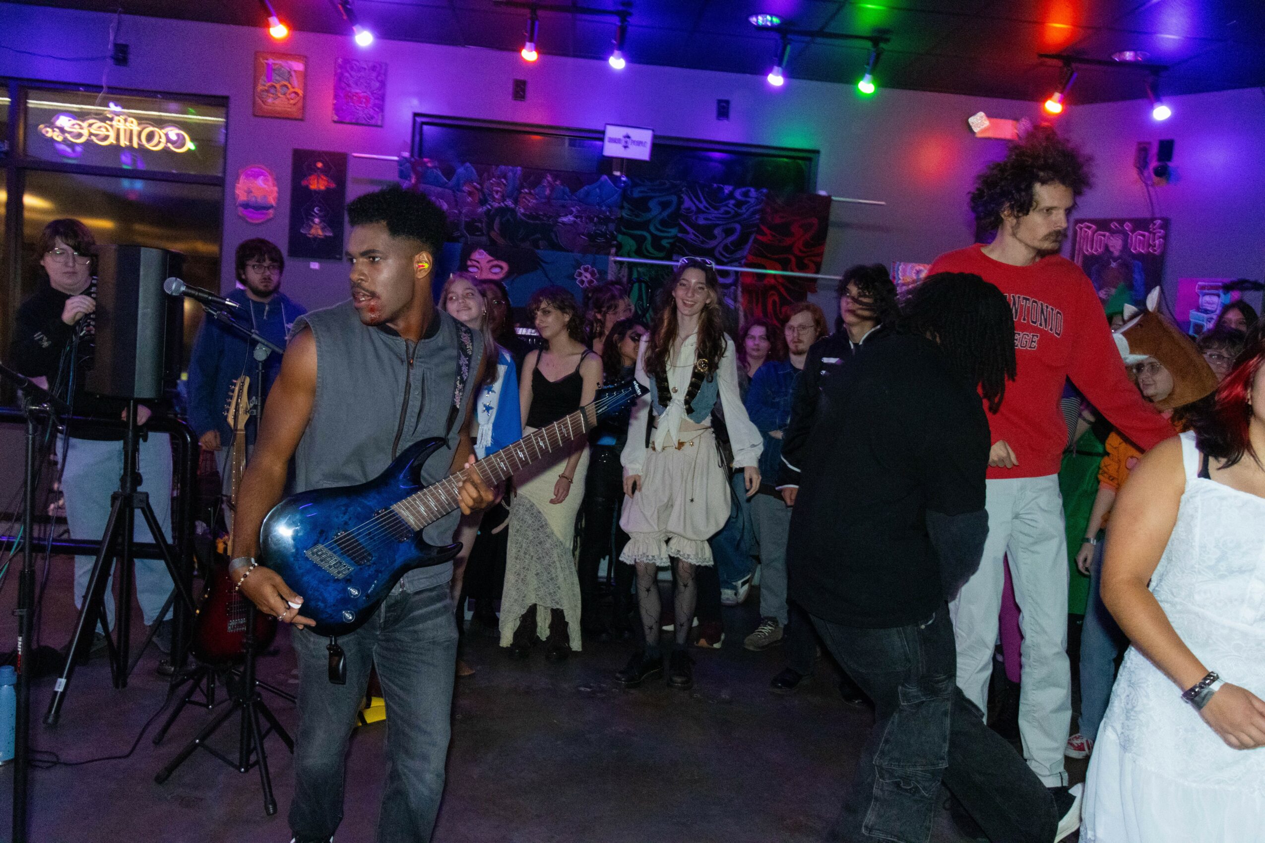 People dancing and socializing in a colorful, decorated indoor venue with neon lights and wall art.