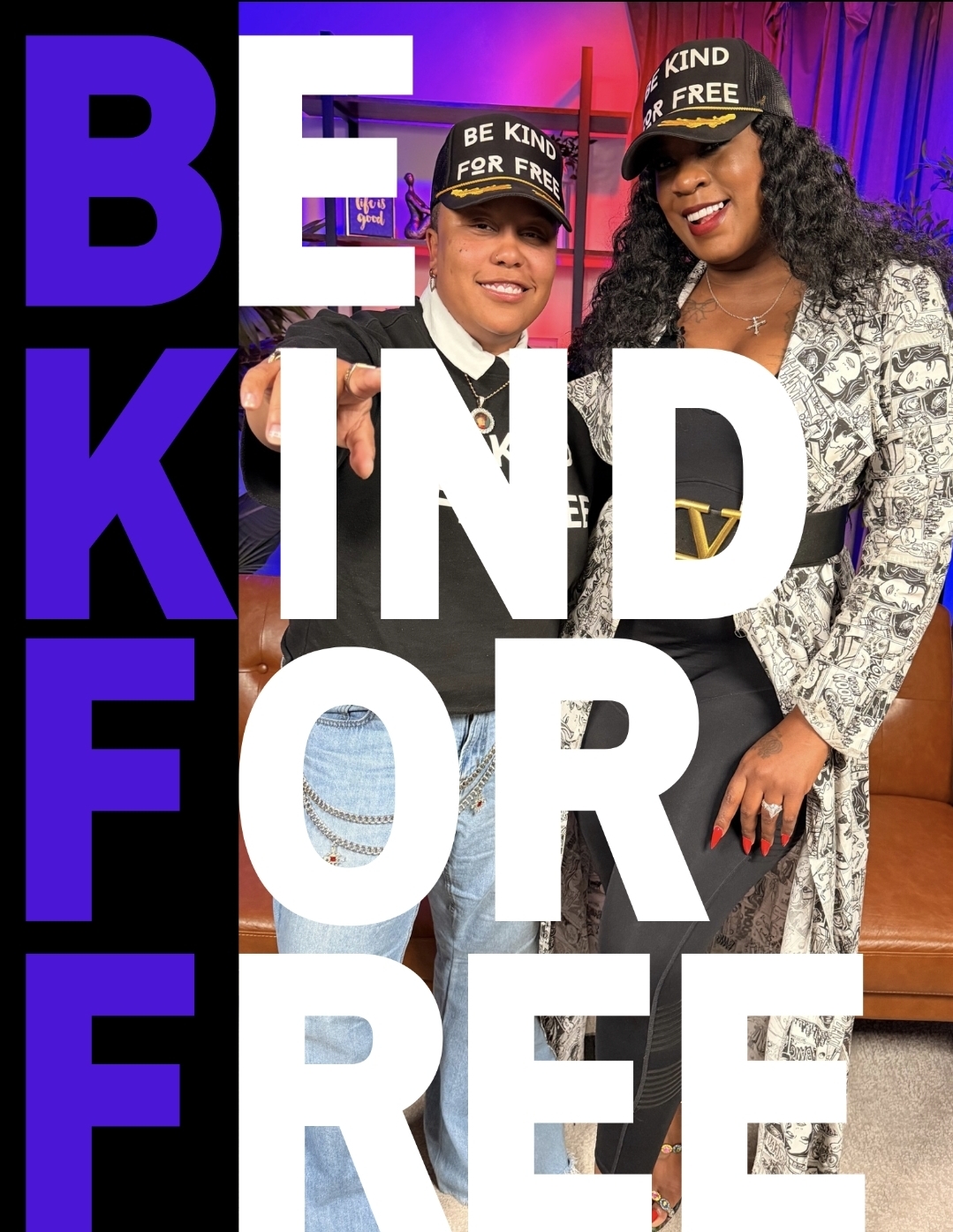 Two women wearing hats with messages, smiling, standing in front of a colorful background with large text reading 'BE KIND FOR FREE'.