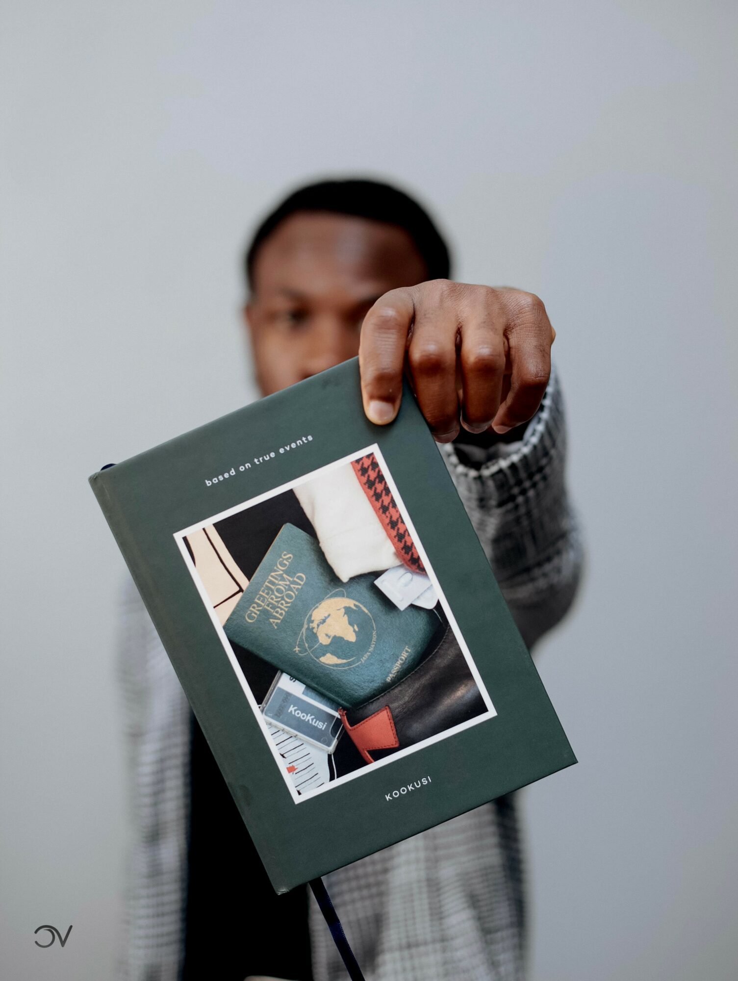 Person holding a book with travel-related items on the cover, facing the camera, against a plain background.