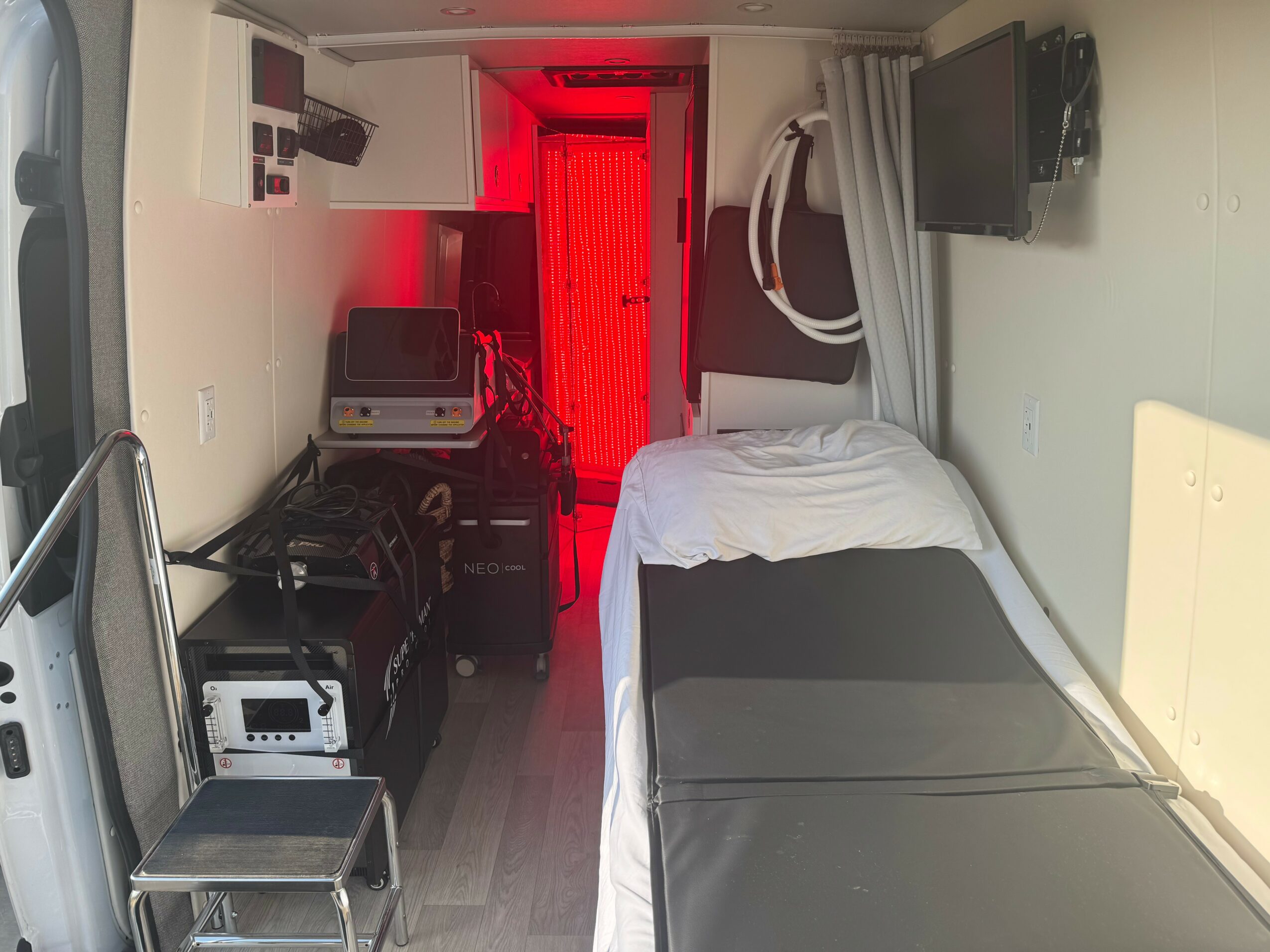 Hospital room with bed, monitor, and equipment, illuminated by red light from doorway, with chair and curtains.