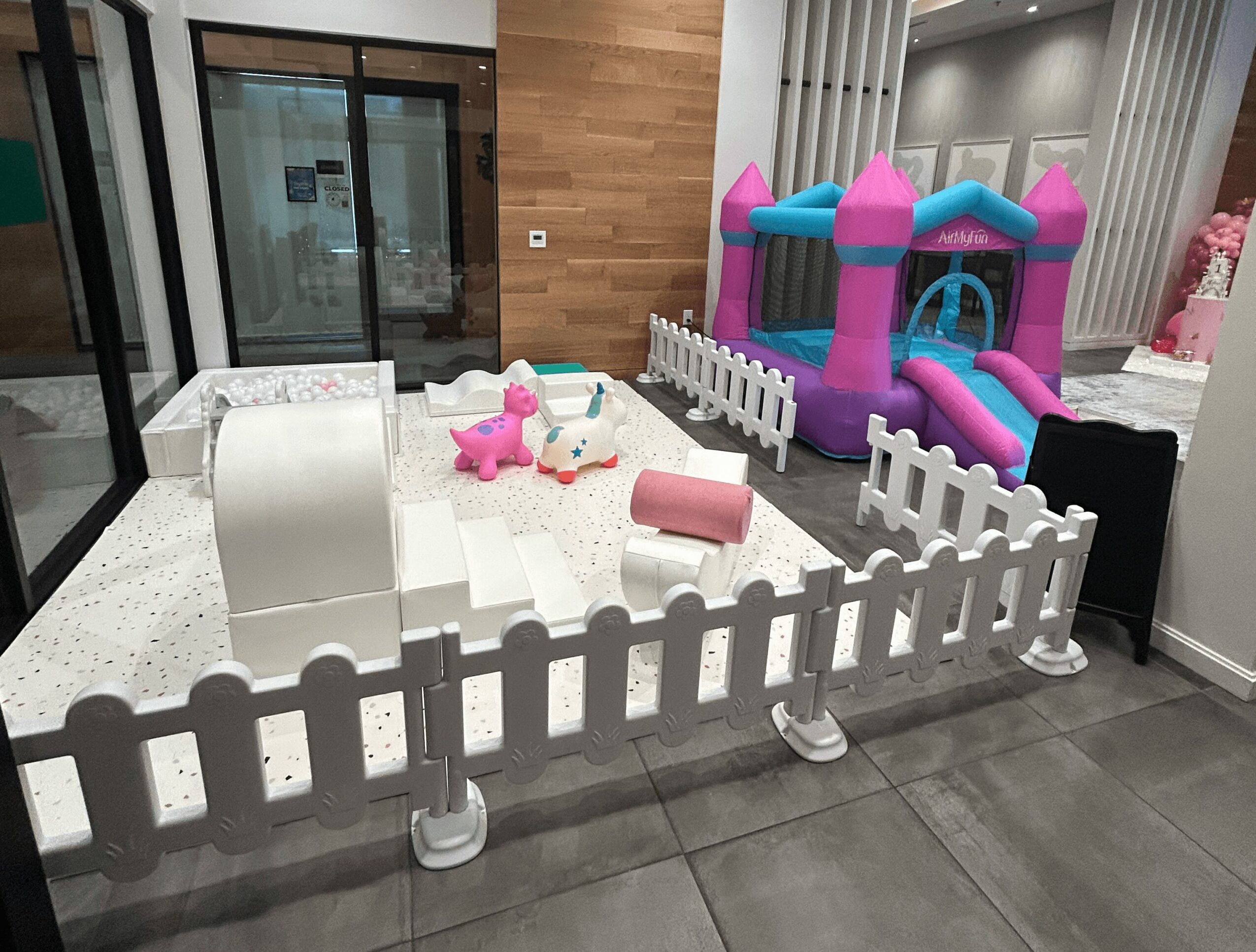 Indoor play area with a white sandbox, pink and white toys, and a colorful inflatable bounce house.