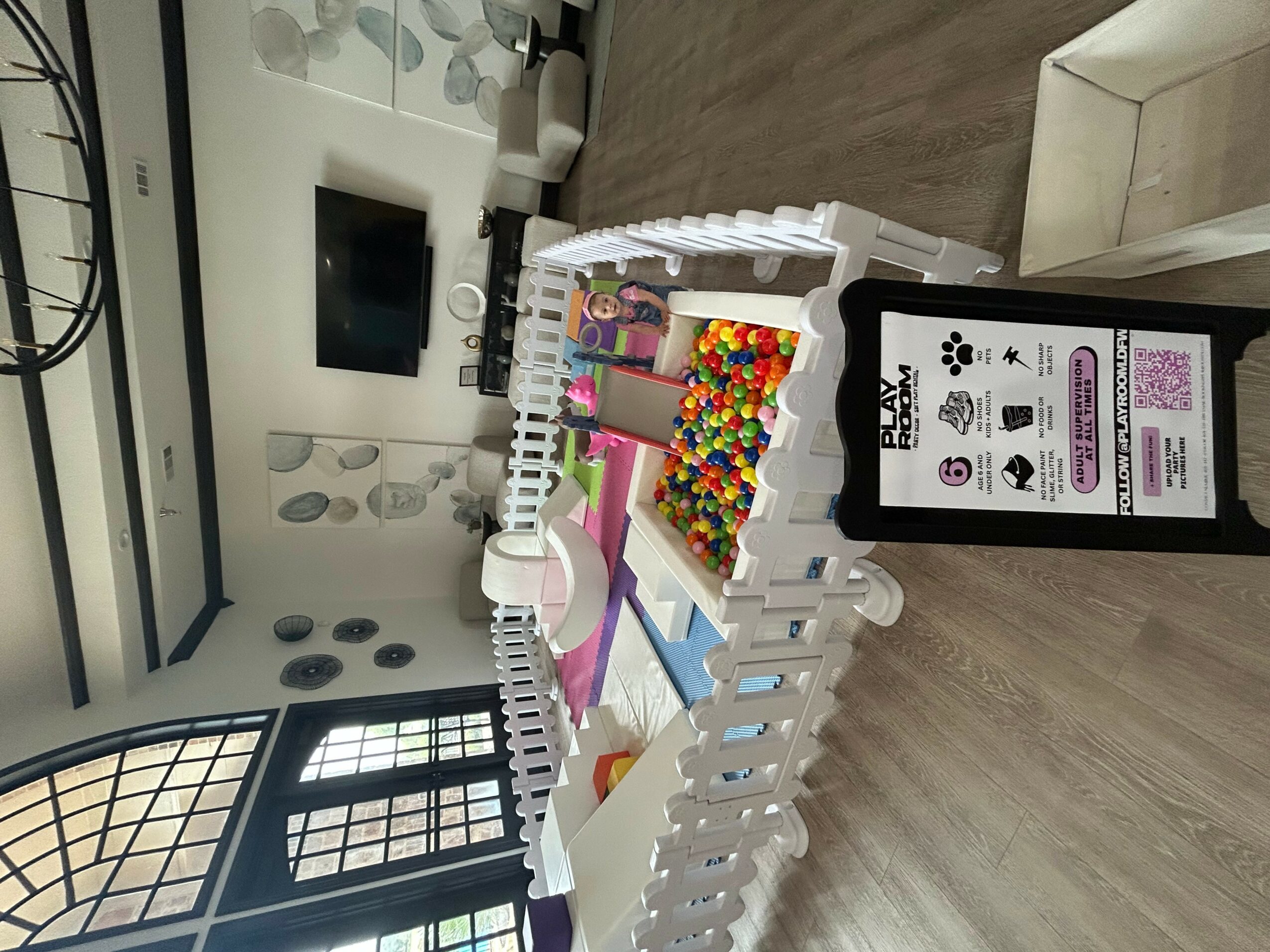 Table with colorful gumballs, paper, and toys, next to a smartphone displaying a QR code, in a room with large windows.