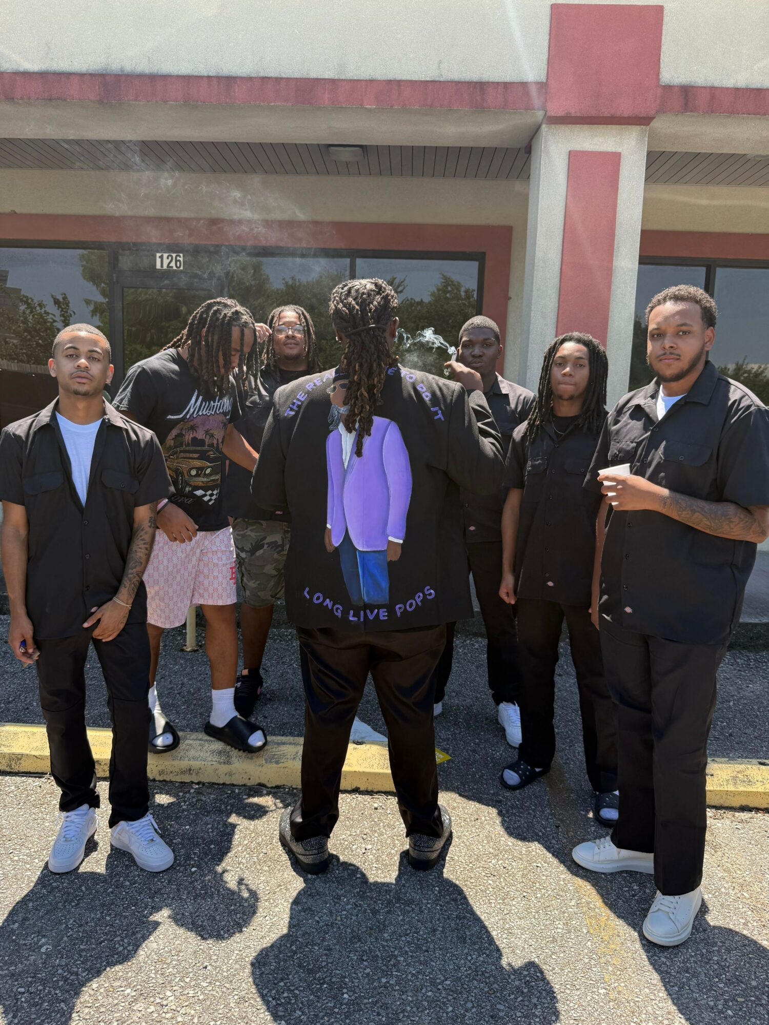 Group of people standing outside a building, some looking at the camera, others talking or looking away.