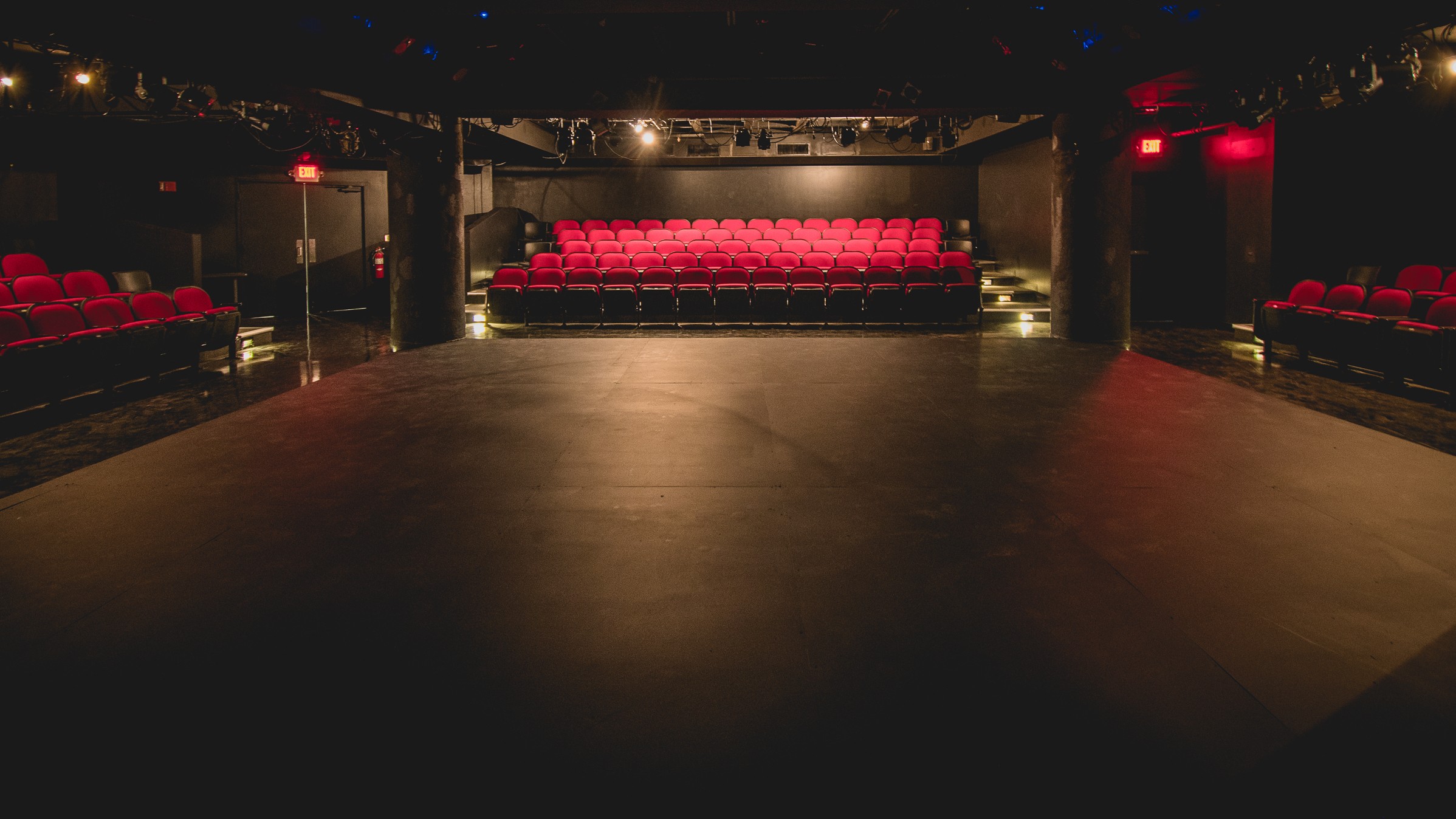 Empty theater stage with red seats in the background and dark surroundings.