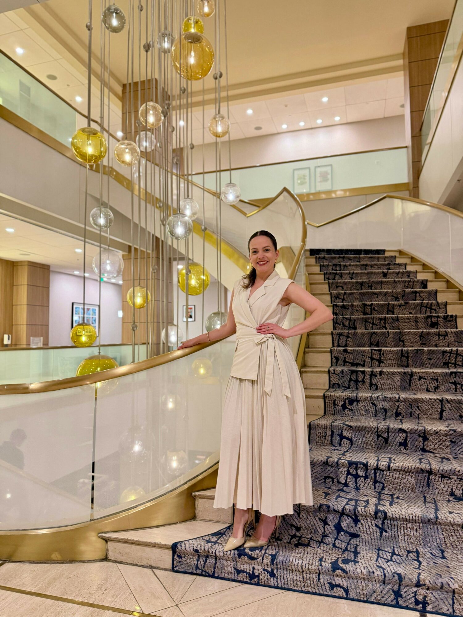 Woman in white dress standing on staircase with decorative hanging ornaments in background.