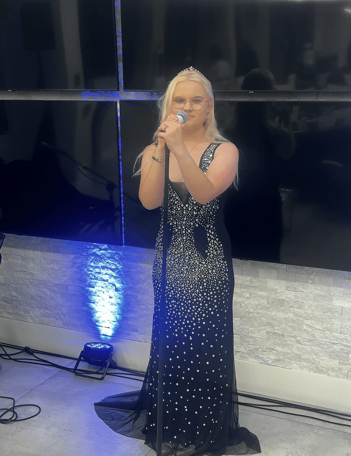 Woman in a black dress with white dots singing into a microphone on stage.